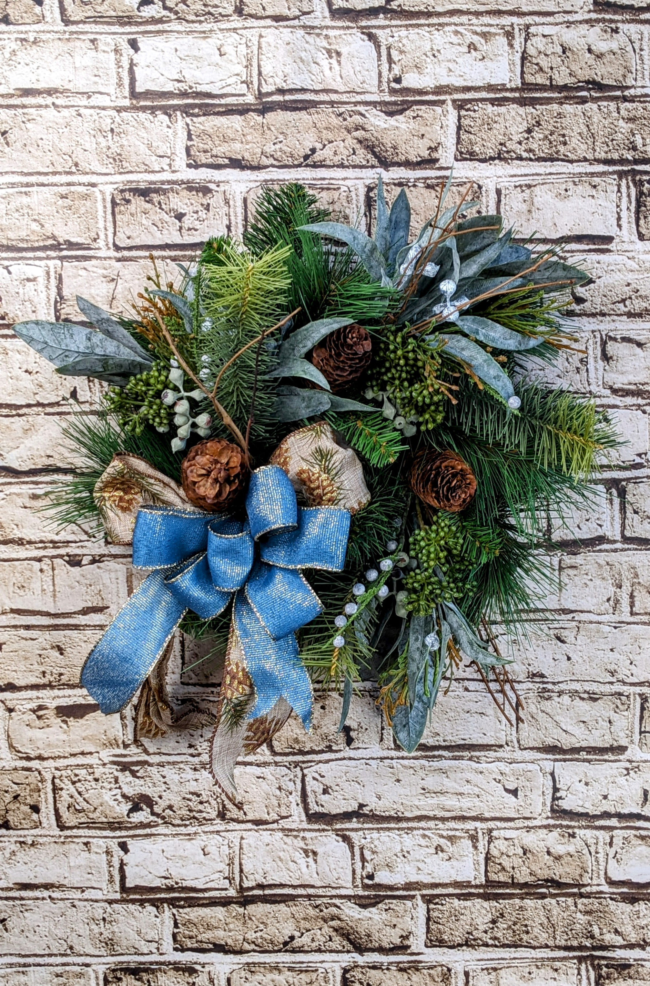 Country Livin' Wreath - 12&quot; Artificial - A charming 12-inch artificial wreath, featuring soft blue hues that evoke a serene, country-like feel. The wreath is adorned with rustic pinecones and an assortment of permanent botanicals, creating a natural, textured look. This smaller-sized wreath is perfect for adding a subtle, seasonal touch to any space, offering a cozy, inviting atmosphere with its understated elegance and rustic charm.  Approximate Dimensions: 12&quot; Diameter