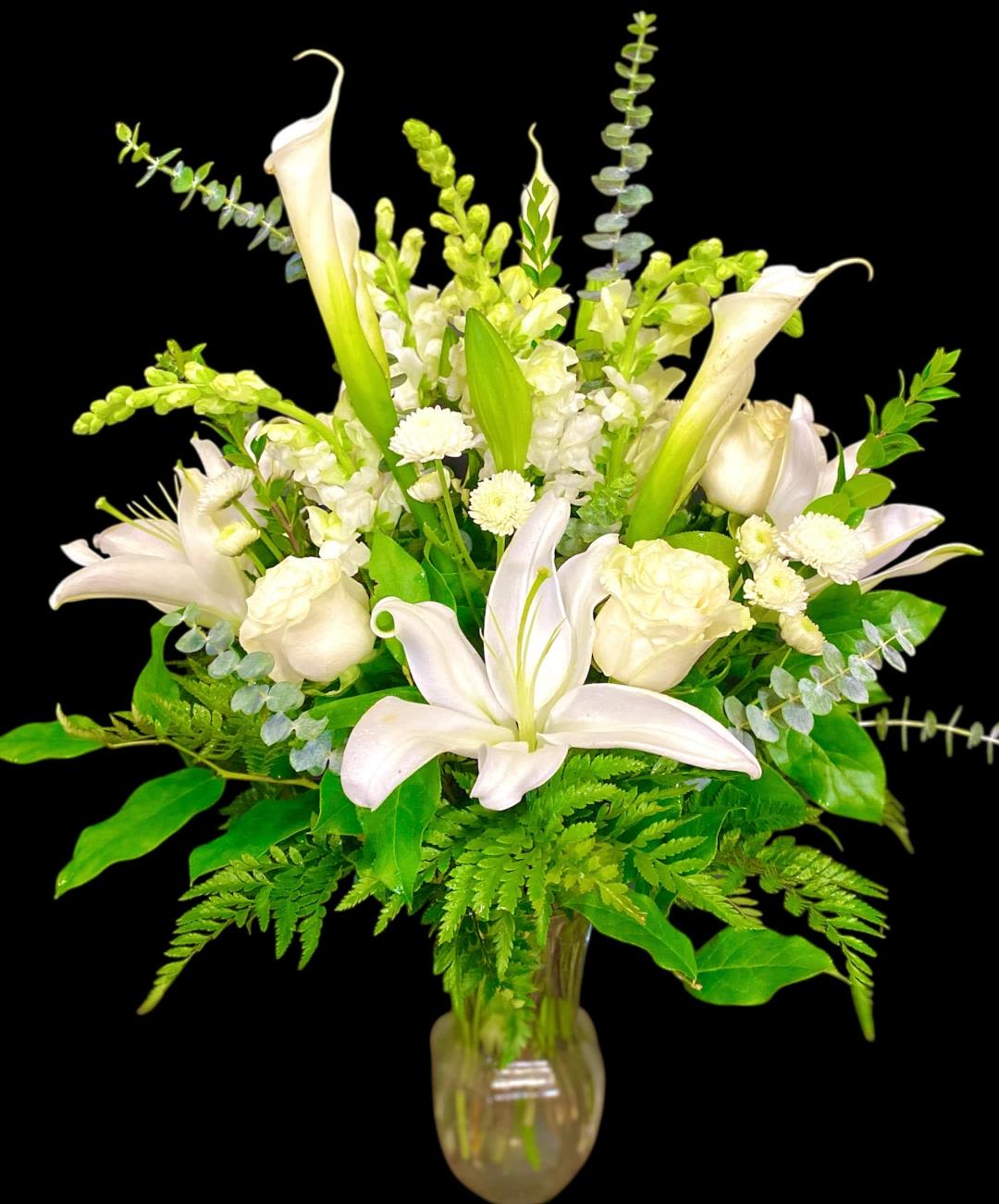 Pure Serenity  - This full lush design includes a variety of white premium blooms to provide the perfect sentiment for just about any occasion. This design includes Roses, Lilies, Snapdragons, Calla Lilies, and Button Mums. These blooms are arranged in a ginger vase and accented with various types of foliage. This design measures approx. 18 &quot;W x 21&quot;H.