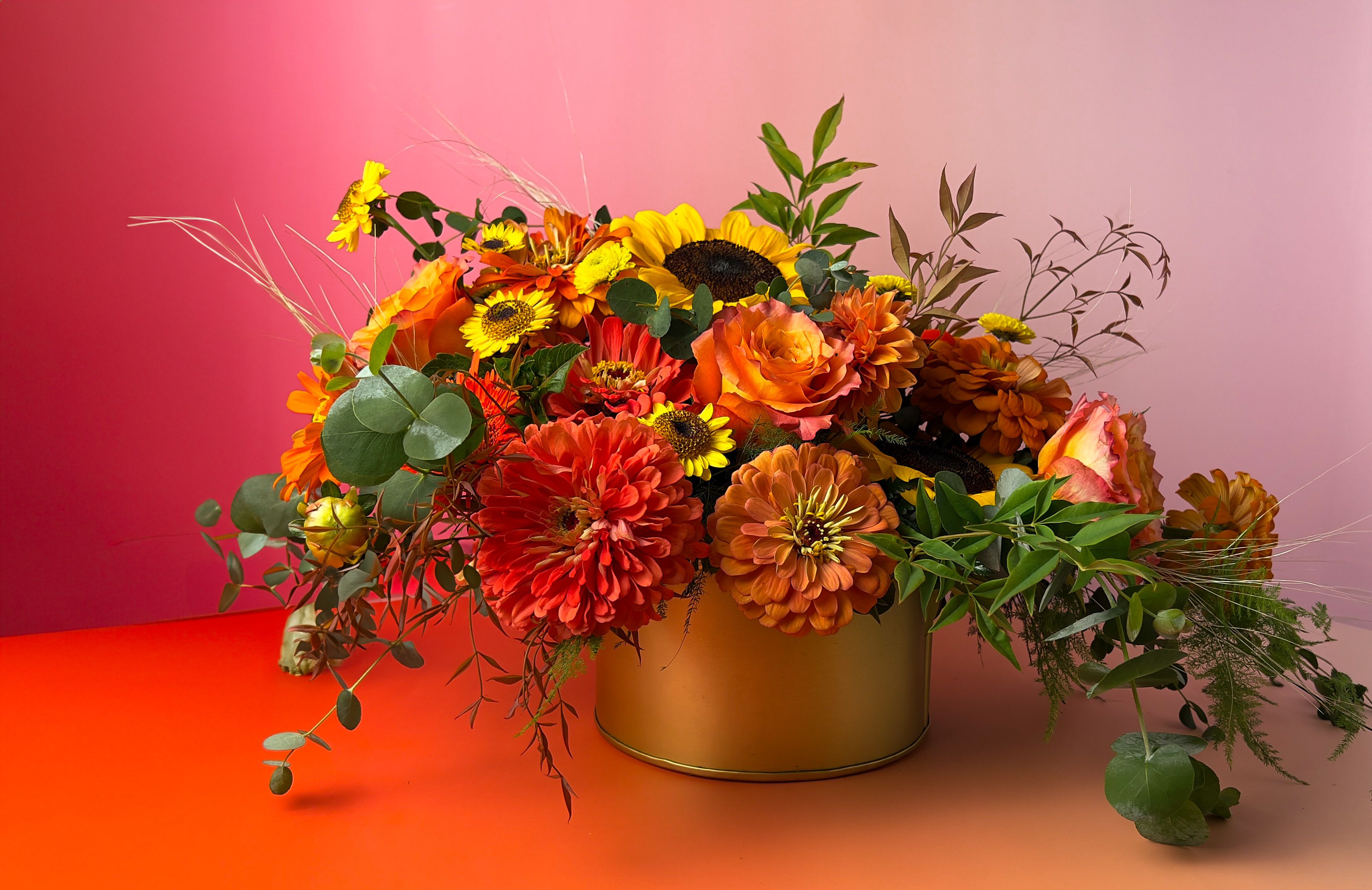 Harvest Blooms Arrangement - Harvest Blooms is a warm and radiant arrangement featuring rich oranges, sunny sunflower yellows, classic reds, and lush greenery. Designed by your trusted Baltimore Florist, The Flower Cart, this vibrant bouquet is elegantly arranged in a gold metal vase, bringing a touch of rustic sophistication and seasonal charm to any space. Perfect for autumn celebrations, birthdays, or simply adding a burst of color to your home or office. Order Harvest Blooms today from The Flower Cart for same-day Flower Delivery in Baltimore and surrounding areas. Each arrangement is thoughtfully handcrafted by our local floral designers to deliver fresh, eye-catching beauty right to your doorstep. 