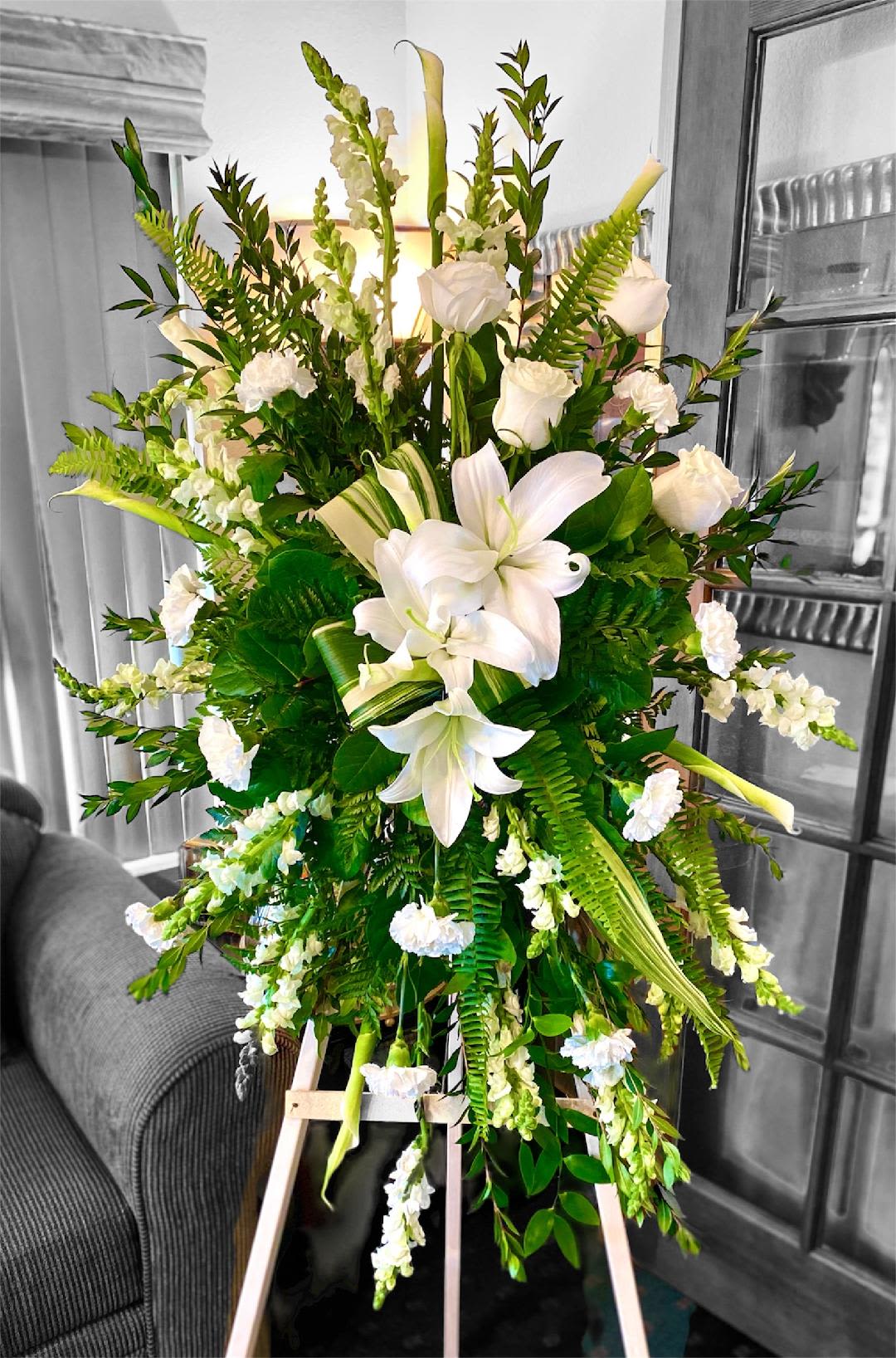 Serene Sympathies Standing Spray  - This simple, yet elegant spray includes a variety of delicate white blooms that send a heartfelt sentiment to your loved one. This design includes Oriental Lilies, Calla Lilies, Roses, Snapdragon, and Carnations. Accented with Variegated leaves and a variety of lush rich green foliage. This design measures approx. 29&quot; W x 50&quot;H. Stand included. 