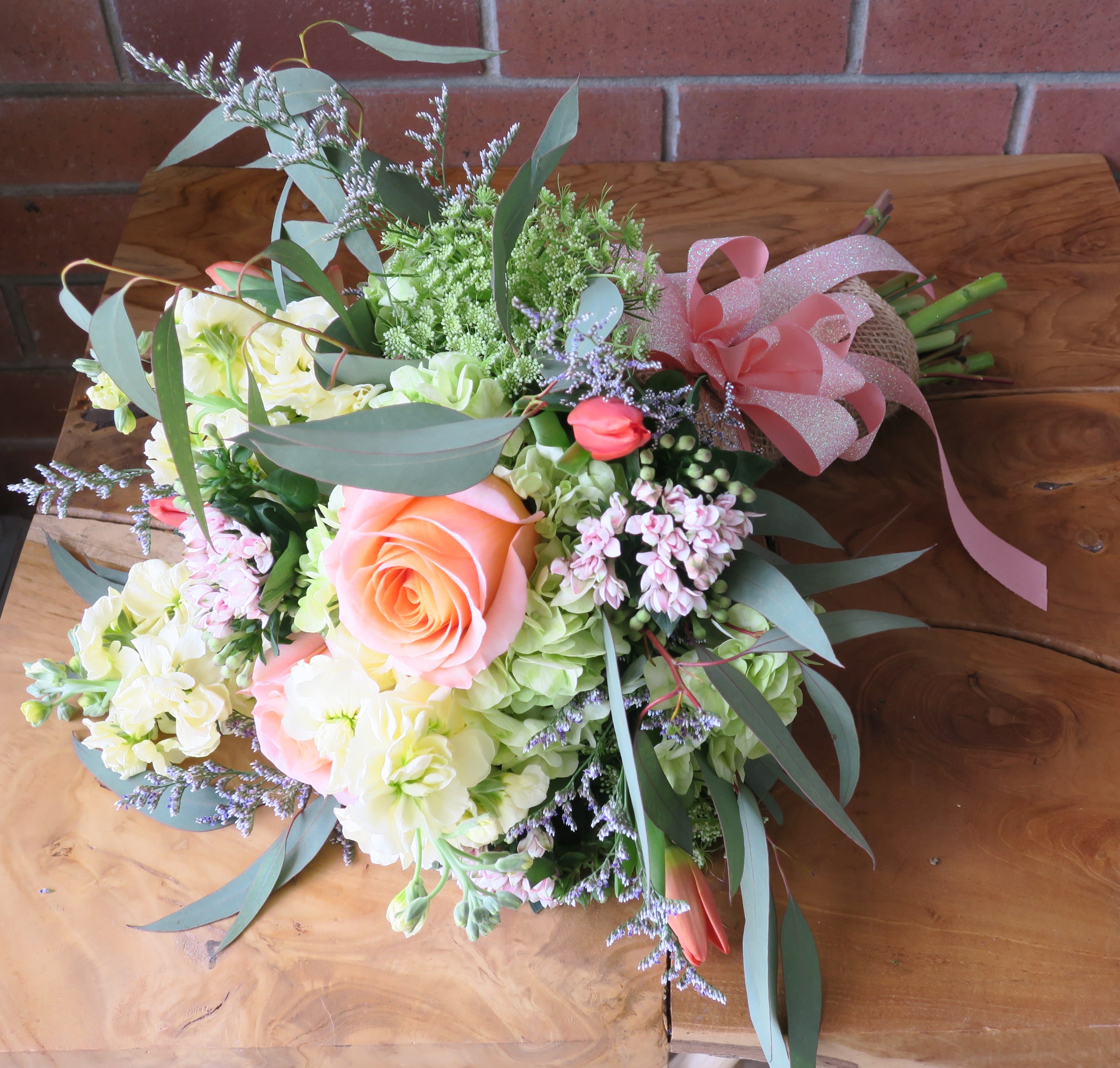 Burlap Wrapped Seasonal Bouquet - Gorgeous coral roses, green hydrangeas, tulips, and other seasonal flowers and fillers wrapped in burlap with a coral bow. 