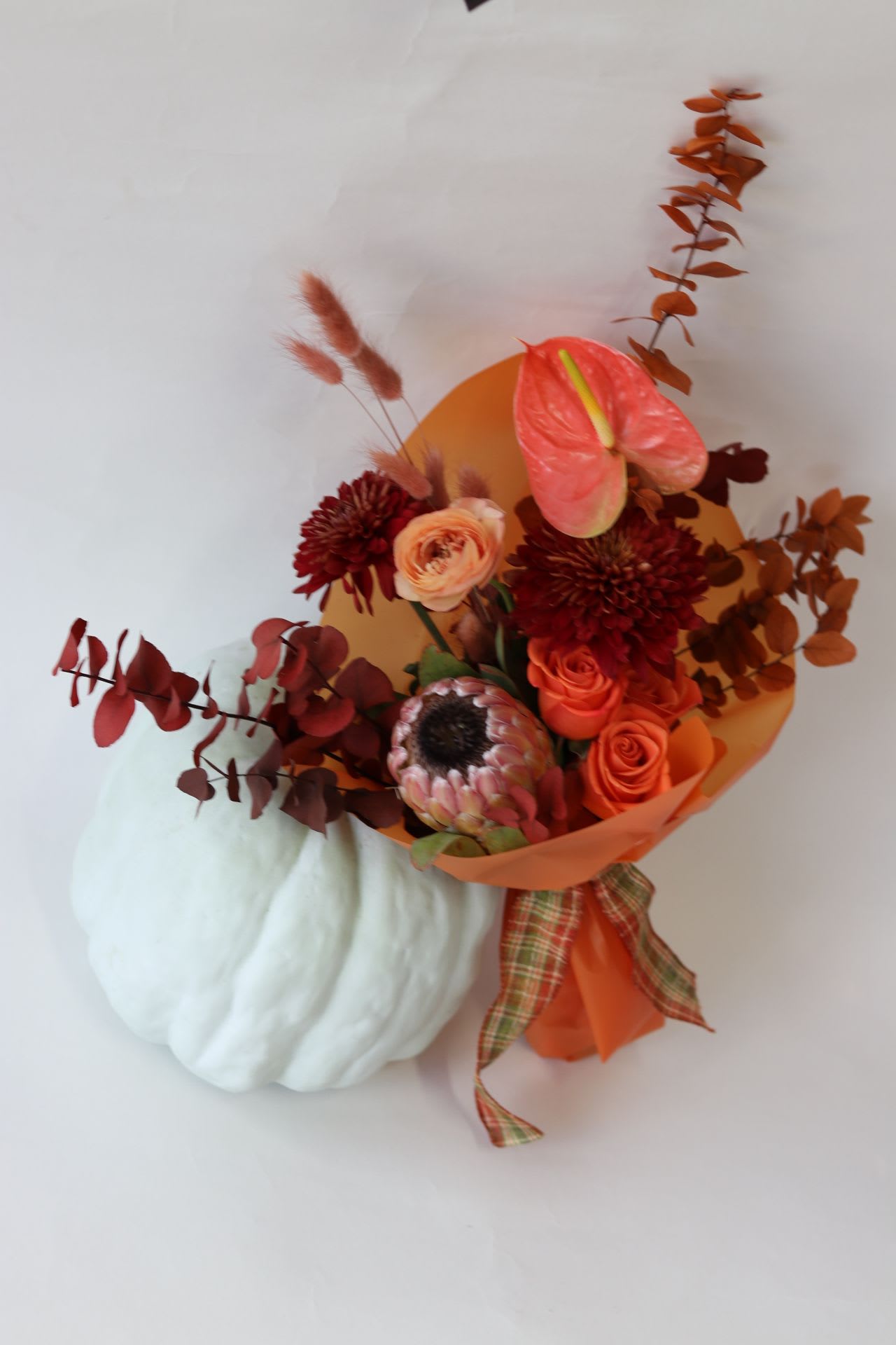 Fall Wrapped Bouquet  - Introducing the Fall Wrapped Bouquet, an exquisite arrangement perfect for anyone who has a vase at home. This stunning bouquet, designed by Venetian Flowers, features a delightful mix of lovely pink ice protea, vibrant orange roses, elegant anthurium, cheerful fall mums, and beautifully preserved fall eucalyptus. Each bouquet showcases a unique blend of colors that may vary slightly, ensuring a one-of-a-kind experience while maintaining the same captivating aesthetic. Whether for a gift or a personal treat, this premium bouquet brings the warm essence of fall into any space, inviting joy and beauty into everyday life.