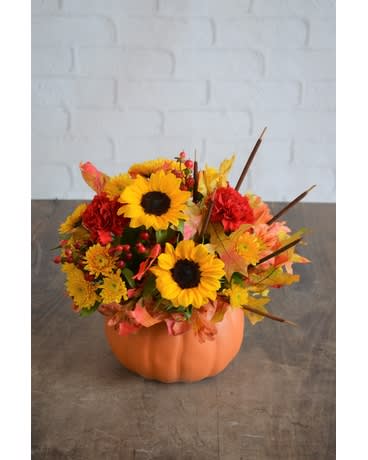 Harvest Pumpkin - Traditionally 'Autumn', this Fall pumpkin features the season's 'signature flowers'. Roses, cattails, hypericum berries and butterscotch poms are richly combined with Fall foliage. The arrangement is designed to be a centerpiece for fall festivities such as Thanksgiving.
