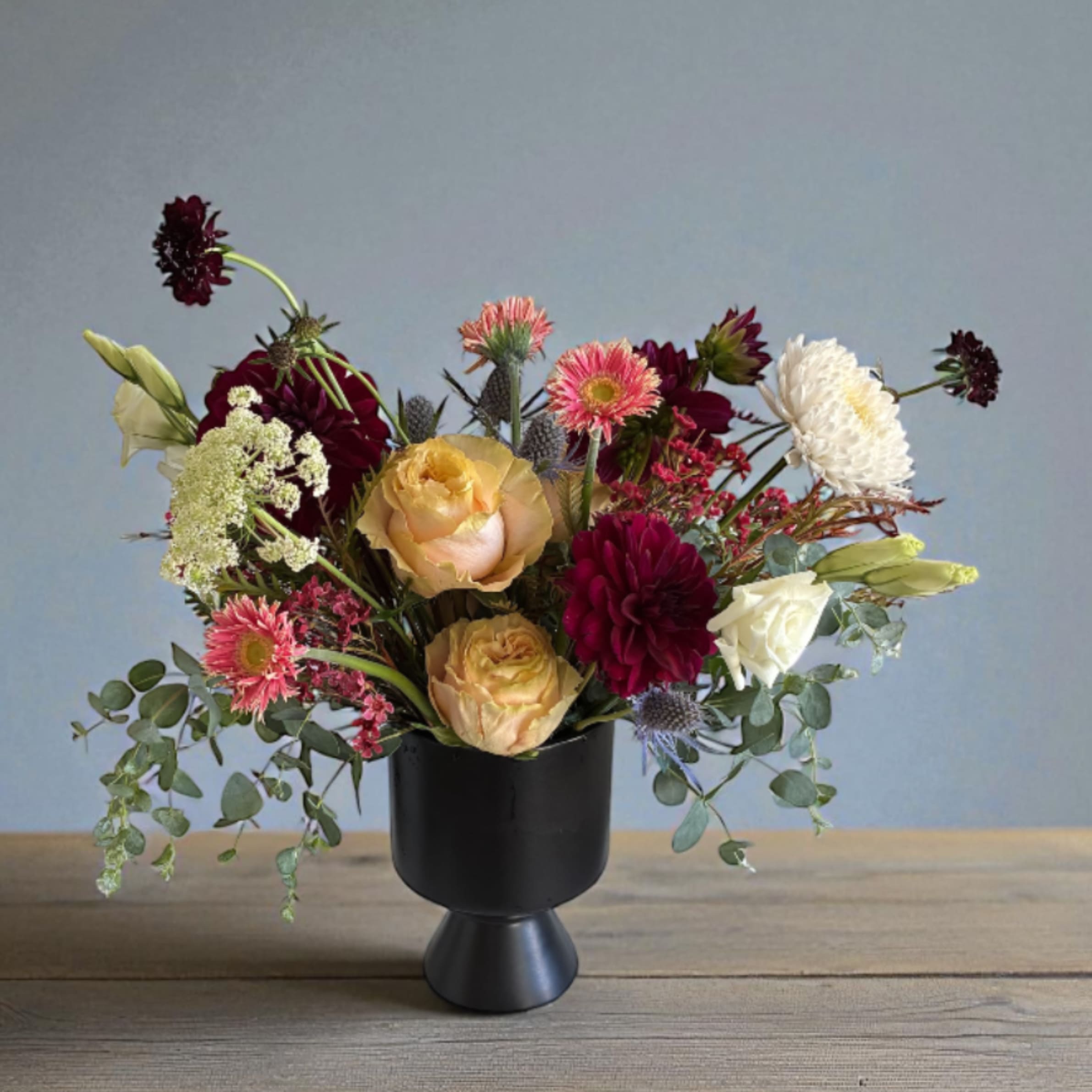 Autumn Jewels - Bring the warmth of the season indoors with this elegant black vase, artfully filled with blooms in rich autumn hues and jewel tones. Deep, rustic reds and soft neutrals come tougher in a stunning seasonal display that perfectly complements the vase's sleek, modern design . This eclectic piece adds bold sophistication to any space. For same day delivery, call at 949-682-5004. Colors and flower may vary from picture based on availability.