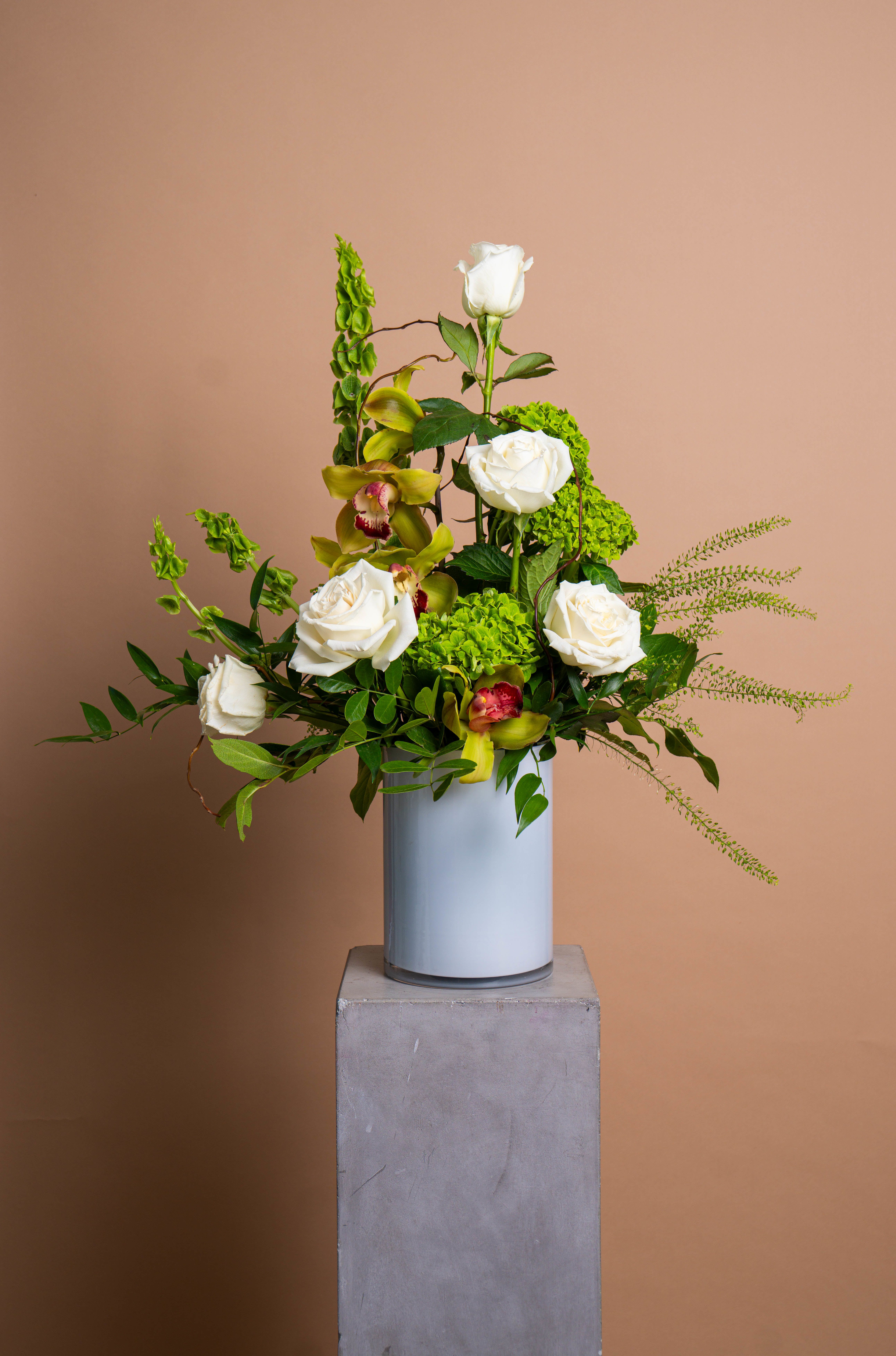 PALOMA - An expression of calm refinement. PALOMA blends white roses, cymbidium orchids, and green hydrangea in a sculptural design that feels both structured and fluid. Each stem is placed to honor space, light, and quiet luxury.  Graceful, modern, and deeply serene, PALOMA captures the essence of effortless beauty.  The arrangement pictured is Deluxe.