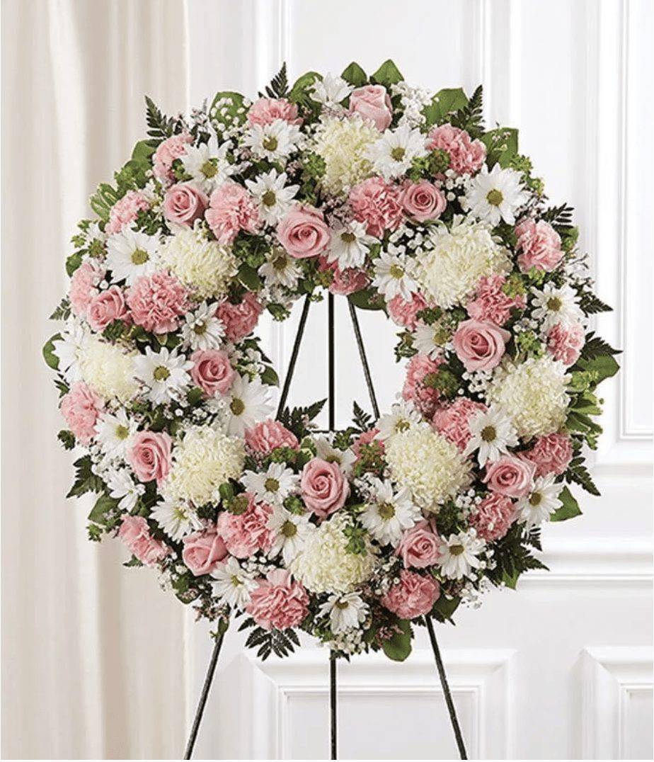 Pink &amp; White Circle Standing Wreath - Celebrate a life with this Pink and White Standing Circle Wreath. The wreath is created with pink roses, pink and carnations, white mums, greenery and more. All the flowers are arranged in a wreath shape, a beautiful gift for a funeral. The deluxe wreath measures approximately 34&quot;H x 34&quot;W without easel and the regular is approximately 30&quot;H x 30&quot;W without easel. The Easel will be delivered with the Pink Sympathy Funeral Wreath, along with a card message.  Includes:&nbsp; • Pink Roses&nbsp; • Pink Carnations&nbsp; • White Mums&nbsp; • White Daisies&nbsp; • Baby's Breath