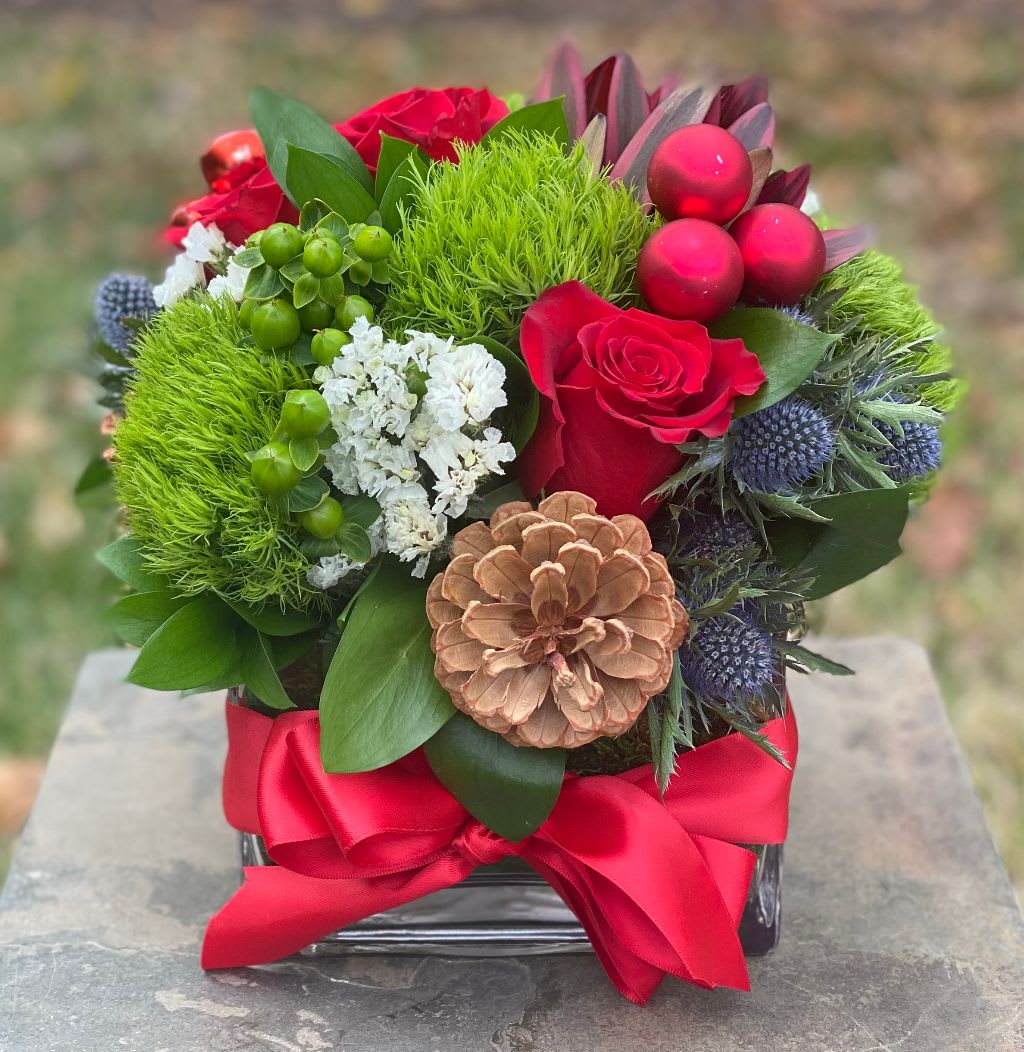 Christmas Kiss - Christmas Kiss – Festive Holiday Floral Arrangement in Wilmington, Delaware  Spread holiday cheer with Christmas Kiss, a vibrant and elegant floral arrangement handcrafted by your local Wilmington, Delaware florist. This festive design features lush green trachelium, classic red roses, textured thistle, striking protea, and sparkling red Christmas ornaments, all artfully arranged in a modern glass rectangular vase and finished with a luxurious red satin ribbon. Perfect for Christmas centerpieces, holiday gifts, or seasonal home décor, Christmas Kiss combines color, texture, and festive charm for a truly memorable holiday display. Each arrangement is made with fresh, premium flowers and is available for same-day flower delivery in Wilmington, DE, and surrounding areas.  Order Christmas Kiss today from your trusted Wilmington florist and bring elegance and holiday spirit to any space this season.