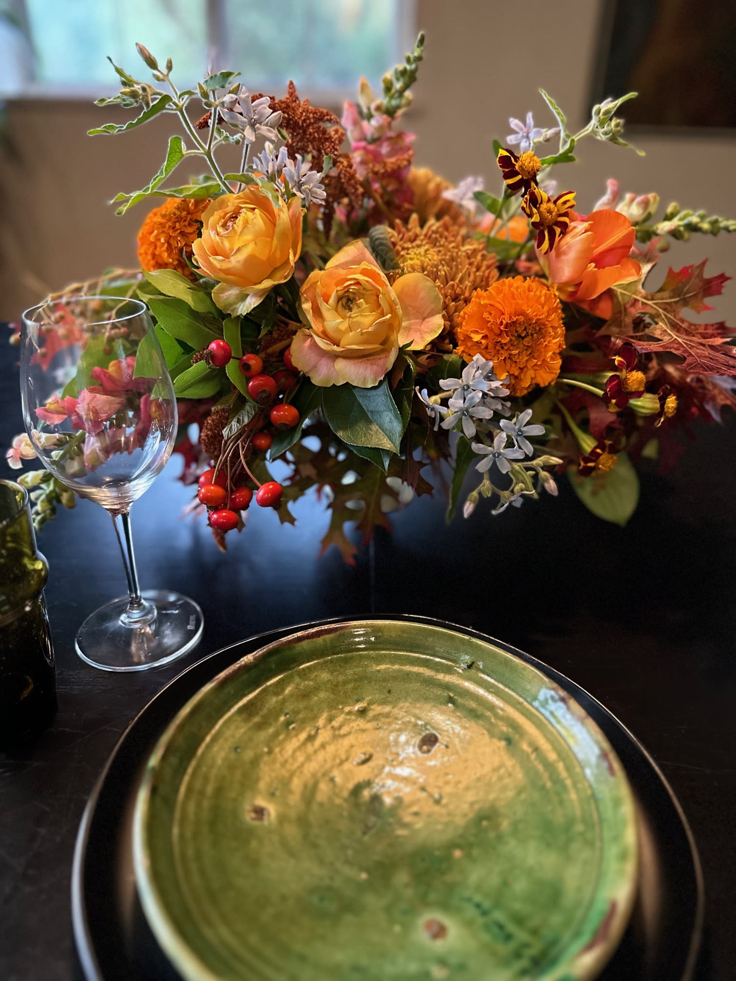 Autumn Table Centerpiece - All the fall colors with a tinge of blue for interest! With flowers such as heirloom mums, garden roses, rose hips, tulip and marigold. This arrangement is double sided and arranged low so guests can see &amp; talk to each other. Clear glass container. Suitable for a 4 place setting table. See our other centerpieces for larger tables.