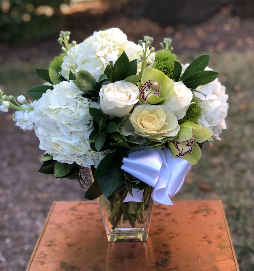 Hydrangea Blooms - Hydrangea Blooms – Elegant White and Green Flower Arrangement | Wilmington, DE Florist  Discover the timeless beauty of our Hydrangea Blooms arrangement, handcrafted by Petals Flowers and Fine Gifts, your trusted local florist in Wilmington, Delaware. This sophisticated design features lush white hydrangea, elegant white roses, vibrant green trichelium, and exotic green orchids, all artfully arranged in a clear glass vase adorned with a delicate white satin ribbon.  Perfect for weddings, anniversaries, sympathy gestures, or simply brightening someone’s day, Hydrangea Blooms is available for same-day flower delivery in Wilmington, DE and surrounding areas including Hockessin, Newark, Chadds Ford, and Kennett Square.  Order online or visit our Wilmington flower shop to experience premium floral design with a satisfaction guarantee. Let us help you send a fresh, modern statement with this stunning white and green flower arrangement.  