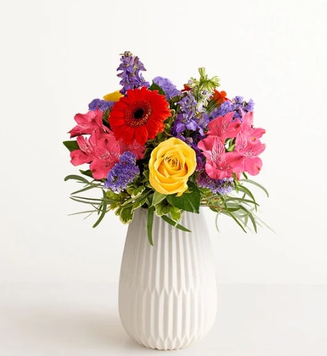 Vibrant Harmony Bouquet - Hit all the right notes with our radiant everyday bouquet. Hand designed by our florists, this harmonious gathering features pops of orange, purple, hot pink and lavender, along with accents of cascading greenery. It’s arranged in our keepsake White Modern Vase, with a tapered design and matte finish that complements the vibrance of every bloom