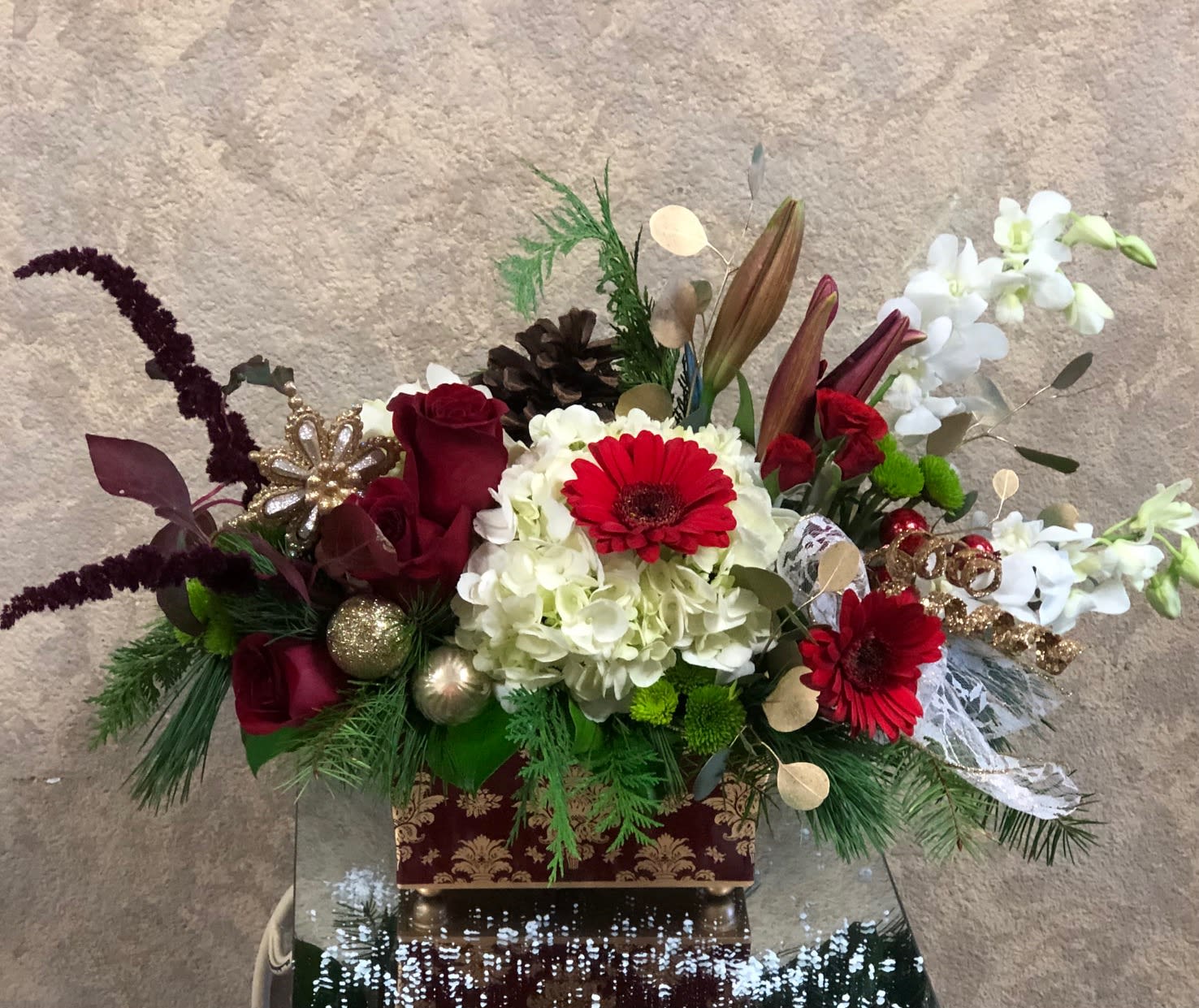 Golden Wishes - Red gerbera, red roses, red lily, white orchids, red spray roses, hydrangea, and green buttons with gold ornaments in gold and burgundy vase.