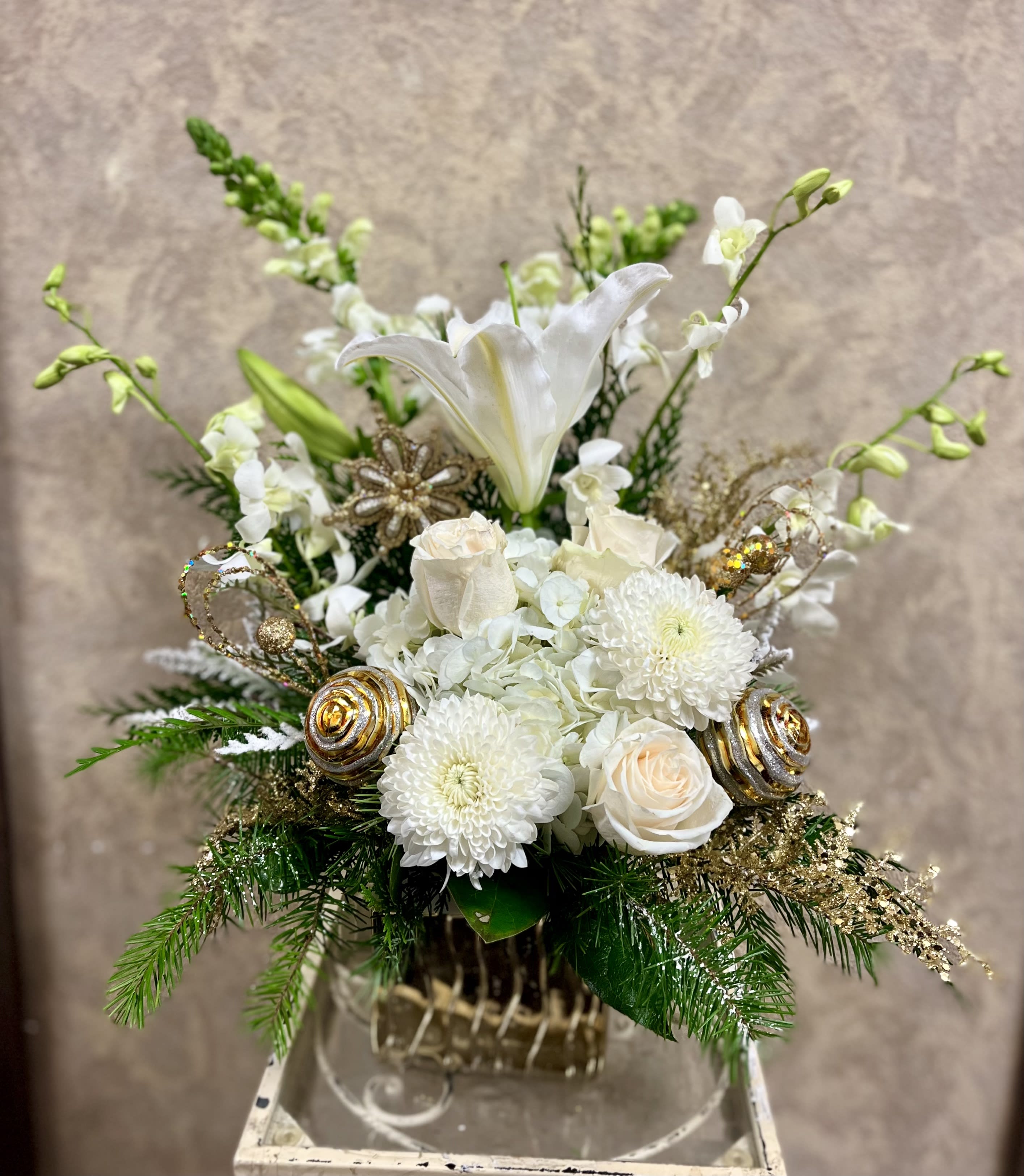 It is the Season to Sparkle - Recipe: White stargazers, White Snapdragons, White Dendrobium, White Roses, Pine branches, Holiday ornaments and accents in a square, golden vase. Availability: All year round Design View: Symmetric Front Facing View Photo shown: Standard 