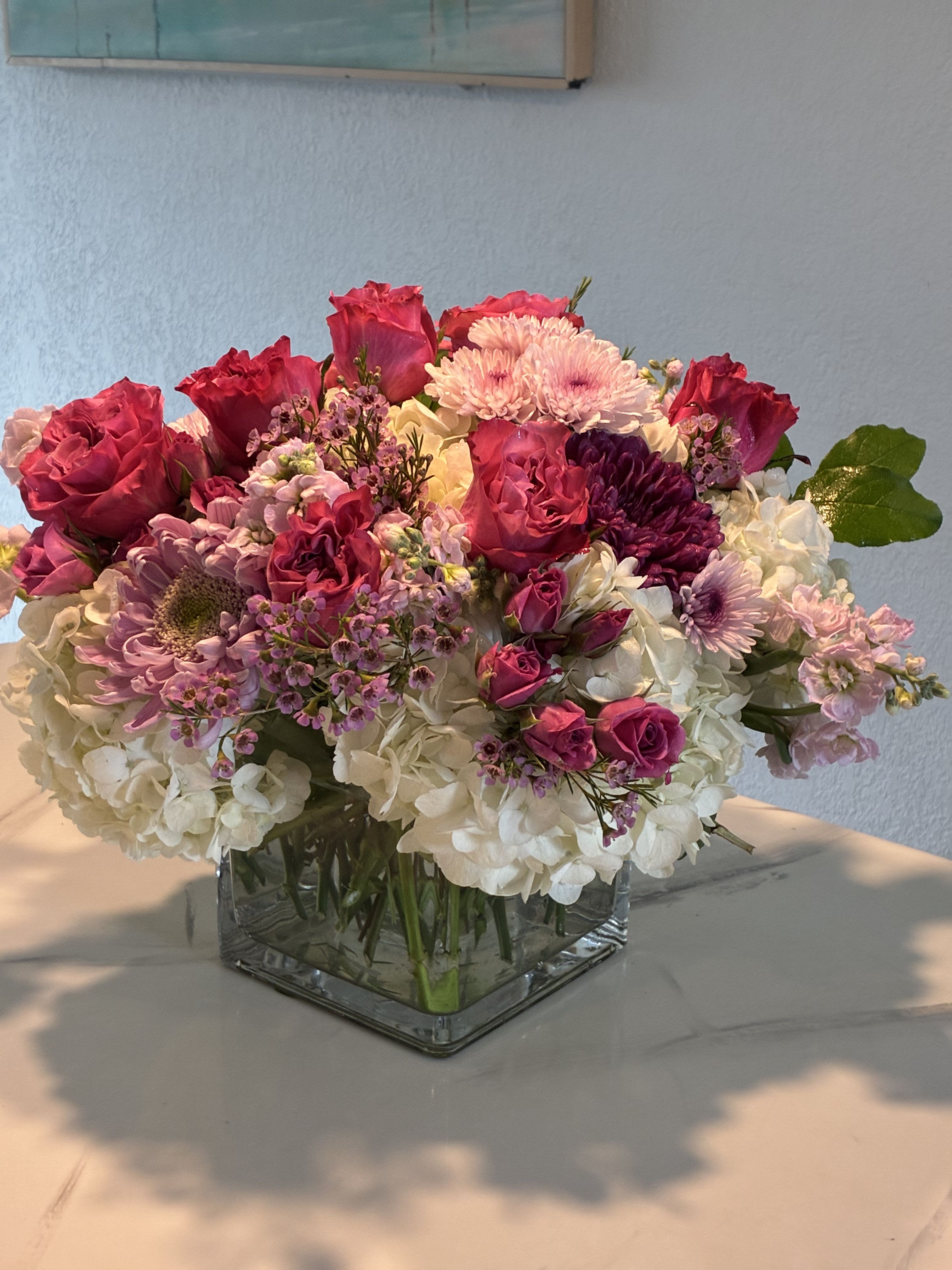 Elegant but mighty - Our unique modern square vase with a mix of purple and pink blooms Delicately placed on a bed of white hydrangea.