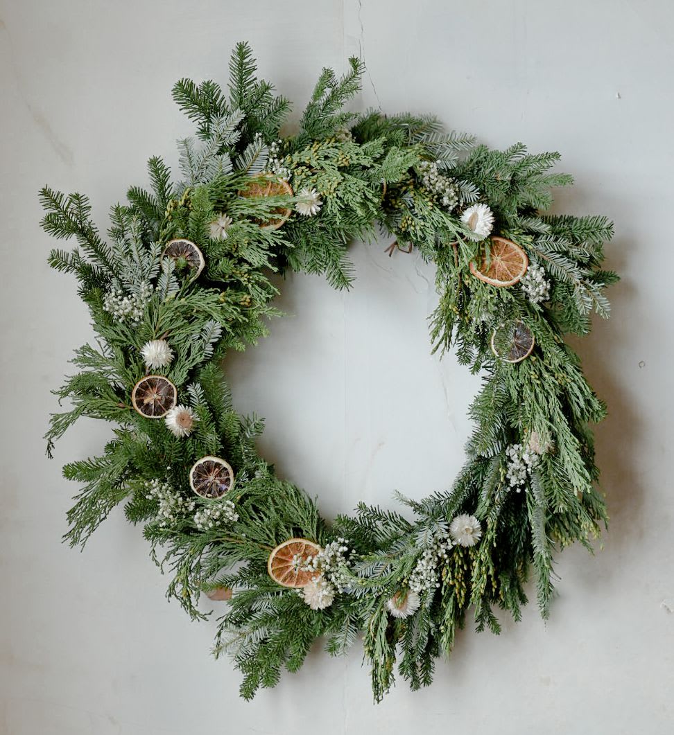 Christmas Green Wreath - A beautiful handmade wreath of assorted evergreens, dried fruits and florals. Please note this is a pre-order. Wreaths will be available the first week of November! Wreaths are made on a base of natural wild grape vine and assembled with wire. Each wreath is handmade and will vary in appearance but reflect the general theme and style pictured. 