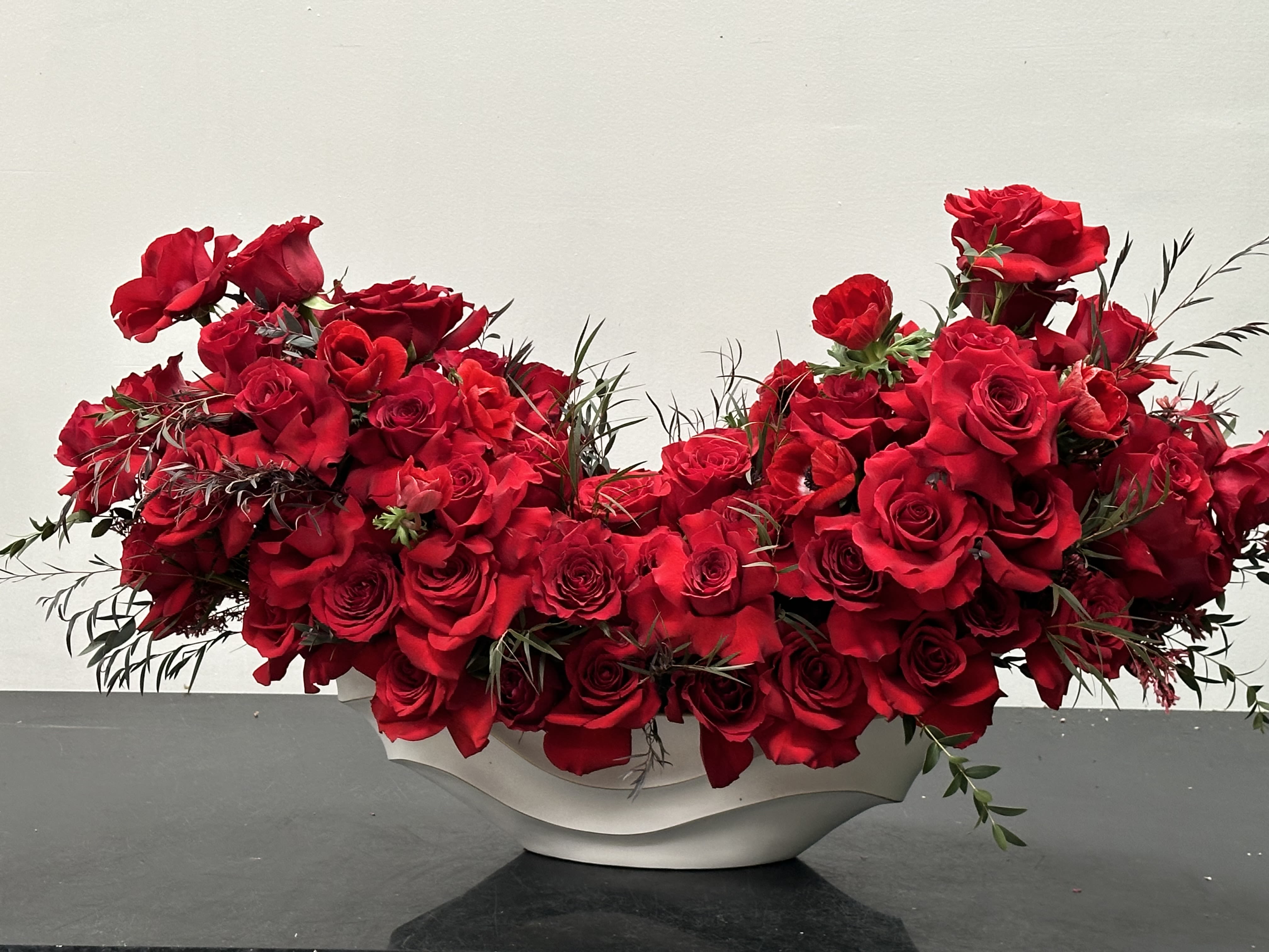 Maria  - Enchanting and dramatic ruby red velvety hues captivates romance and passion. Asymmetric design full and dense of red roses rests in a stunning ceramic white boat vase perfectly showcased in any setting. Maria is stunning and will leave a lasting impression.   Some florals are seasonal, if particular flower will not be available due to season, we will substitute for similar flower, composition, color pallet and value of the arrangements as closely as possible. All effort to create a floral arrangement as close to the photo shown, the actual arrangement may vary slightly in its appearance from the photo shown. If you have any questions about your order, we welcome you to call us in or email   