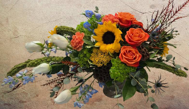 Autumn Radiance Centerpiece - Elevate your autumn gatherings with the Autumn Radiance Centerpiece. A stunning display of warm orange roses, rich burgundy blooms, sunny yellows, and creamy whites, accented with natural textures like lotus pods and eucalyptus. This arrangement captures the essence of fall with its vibrant hues and organic charm.   Flowers may vary from what's pictured, but the colors and style will reflect the look and will always be filled to value. 