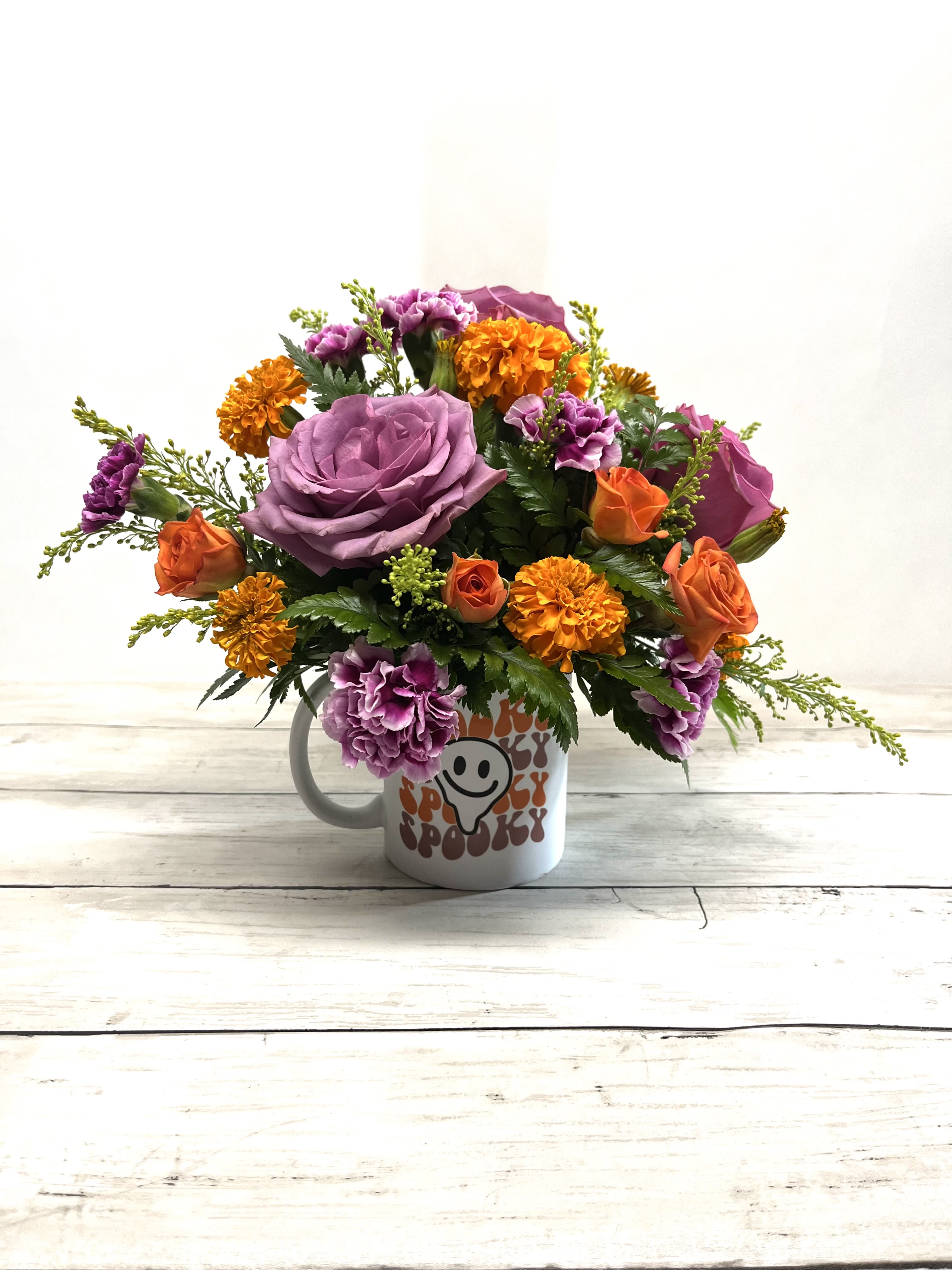 Spooky Halloween Floral Mug Arrangement - Embrace the Halloween spirit with this spooky floral mug arrangement featuring vibrant orange and purple blooms. Designed in a Halloween-themed ceramic mug, this festive piece combines Ecuadorian roses, marigolds, and fall poms with seasonal filler for a playful yet elegant touch. Perfect as a Halloween gift, desk decoration, or a festive home accent, this arrangement brings color and charm to any space. Once the flowers fade, reuse the keepsake mug to enjoy your favorite hot beverages all season long!  Includes: Seasonal fresh flowers in orange, purple, and yellow tones Halloween sublimated mug (designs may vary) Reusable keepsake container  Perfect for Halloween parties, fall birthdays, or spooky-season gifting!  