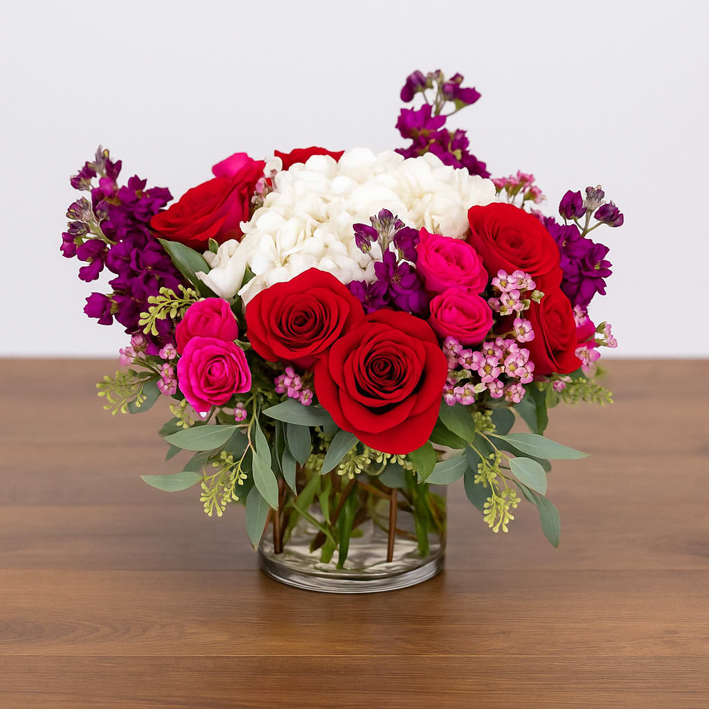 Love Always - Love Always — A romantic and vibrant arrangement designed to make a lasting impression. Featuring lush red roses, fuchsia spray roses, white hydrangeas, and deep purple stock, this bouquet embodies passion and elegance. Handcrafted in a clear glass vase, Love Always is perfect for anniversaries, Valentine’s Day, or any heartfelt occasion. Its bold colors and soft textures create a stunning centerpiece that speaks the language of love.