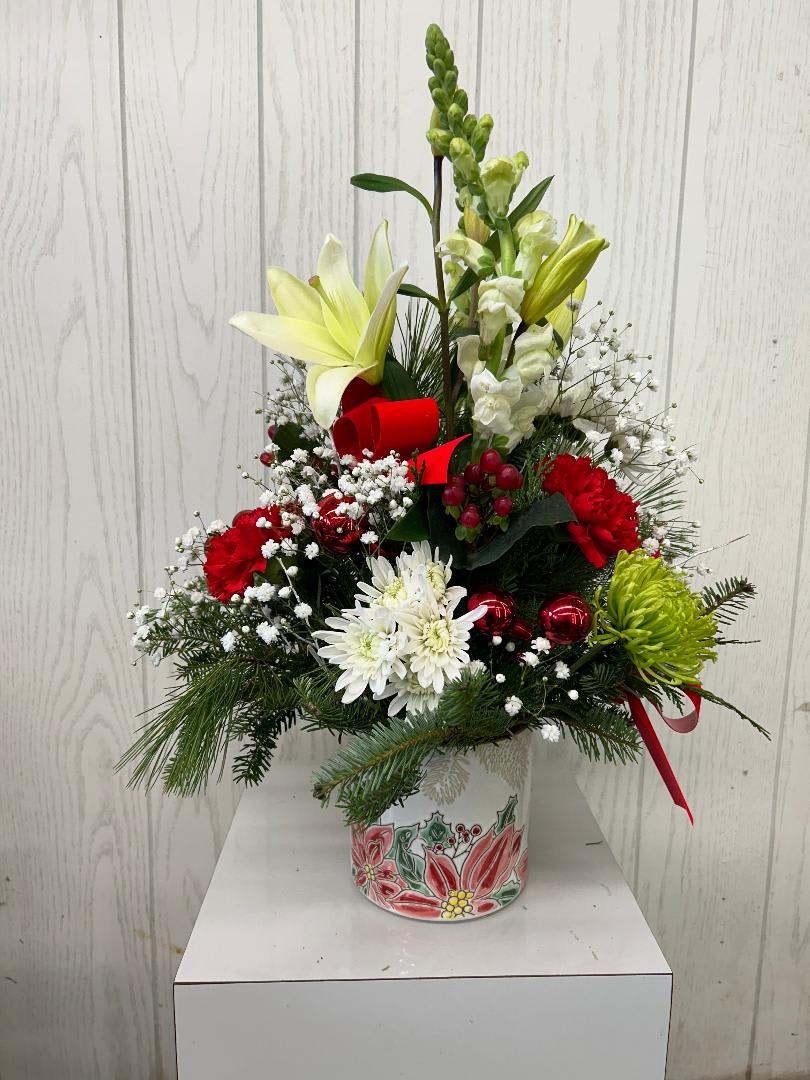 Holiday Happenings Arrangememnt - Celebrate the season with this festive arrangement of holiday classic flowers &amp; Christmas greens. Accented in a ceramic poinsettia themed container. Flower substitutions may be required based on current inventory. Deluxe and premium include red roses.