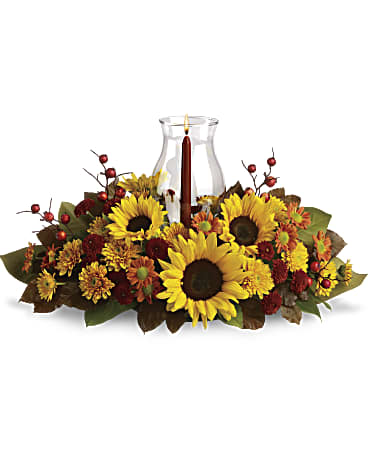Sunflower Centerpiece Arrangement - Sunflowers are the stars of this fabulous fall flower centerpiece! All the classic autumnal colors are here, plus a glowing glass hurricane to make it a heartwarming decoration for your holiday table. Approximately 21 inches wide and 12 inches tall for the Standard size.