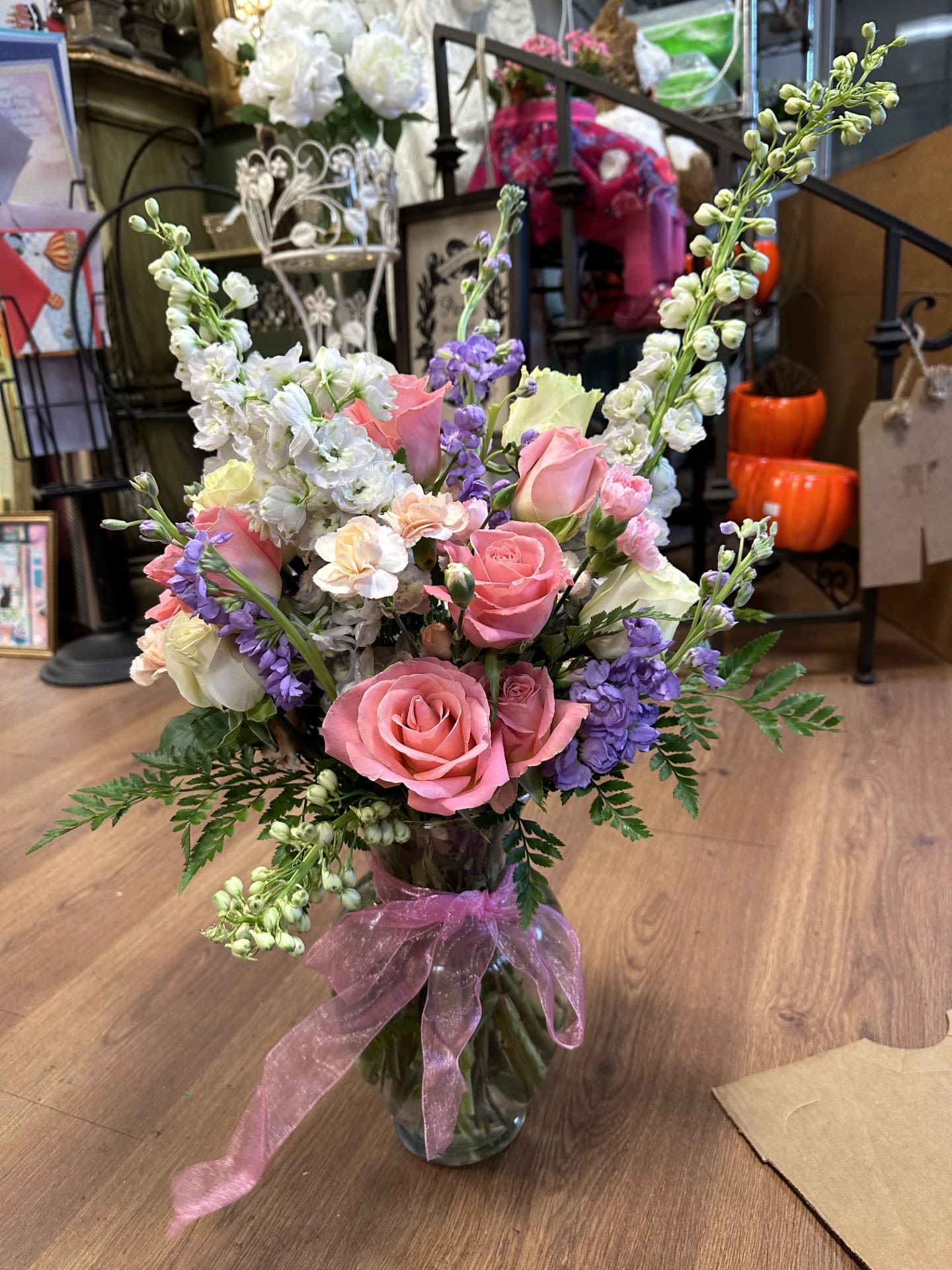 SUMMER ROMANTIC BLISS - A ROMANTIC BOUQUET OF ROSES, DELPHINIUM AND STOCK WITH MIXED GREENS AND A PINK BOW. A TIMELESS BOUQUET