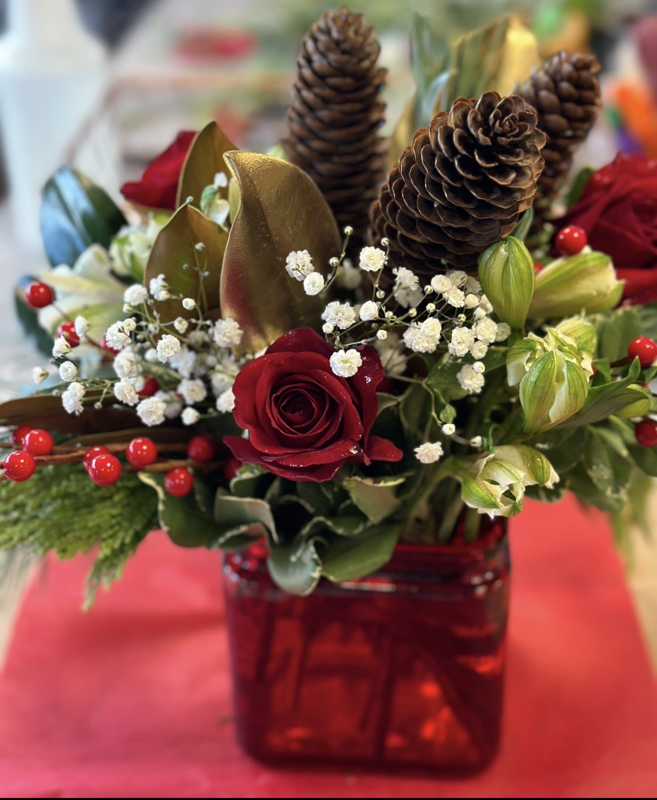 PINECONE SURPRISE CUBE - A RED CUBE FILLED WITH CHRISTMAS/WINTER GREENS, GOLD MAGNOLIA LEAVES,  ALSTROMERIA, BERRY PICKS, PINECONES AND BABIES BREATH A FESTIVE ADDITION TO YOUR HOLIDAY