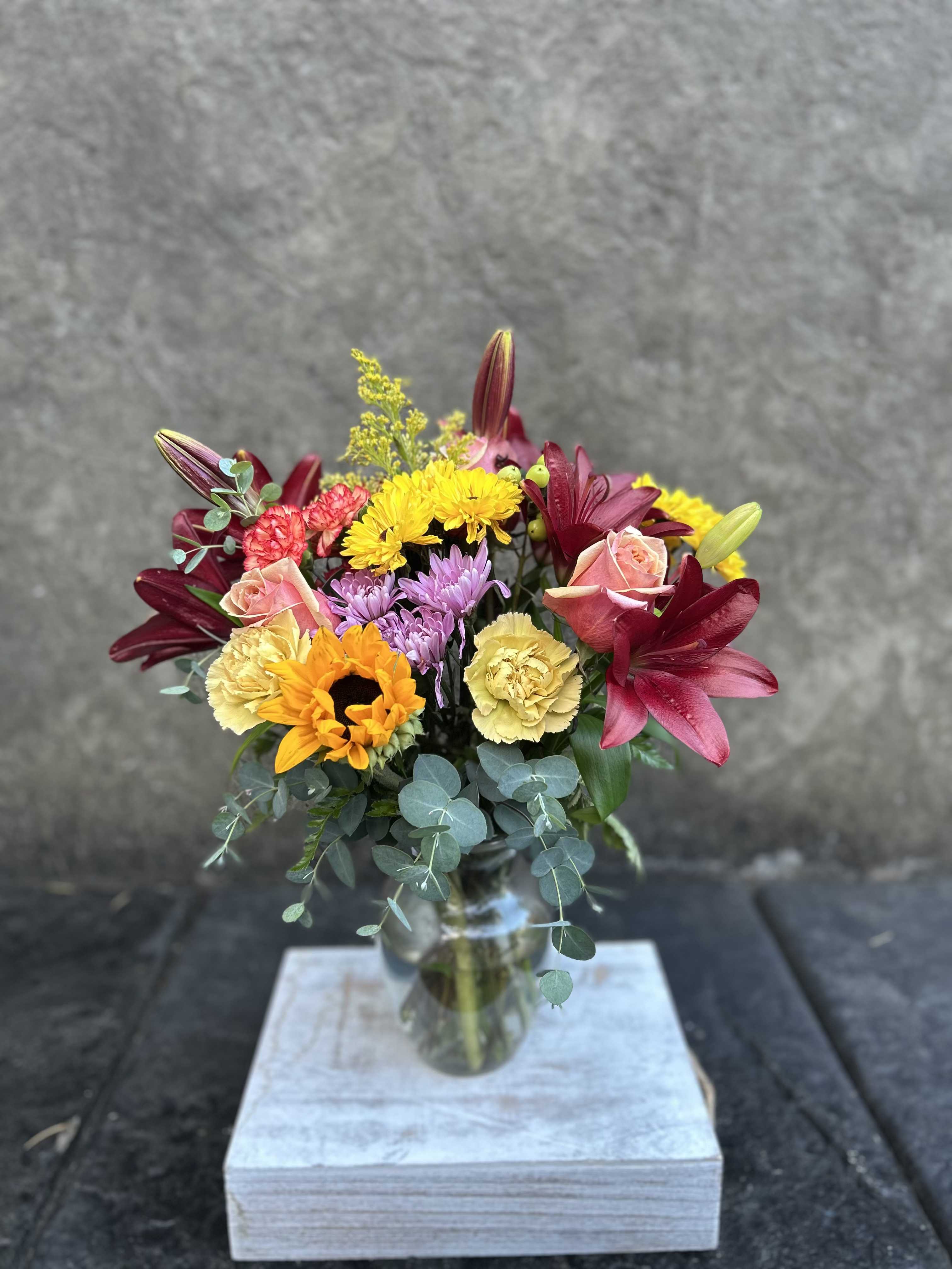 November - Burgundy Asiatic lilies, carnations, mini carnations, chrysanthemums, mini sunflower, sunflowers, roses, and eucalyptus with blooming fillers.  *Reasonable substitutions may be made due to floral availability. Will have overall look and theme.