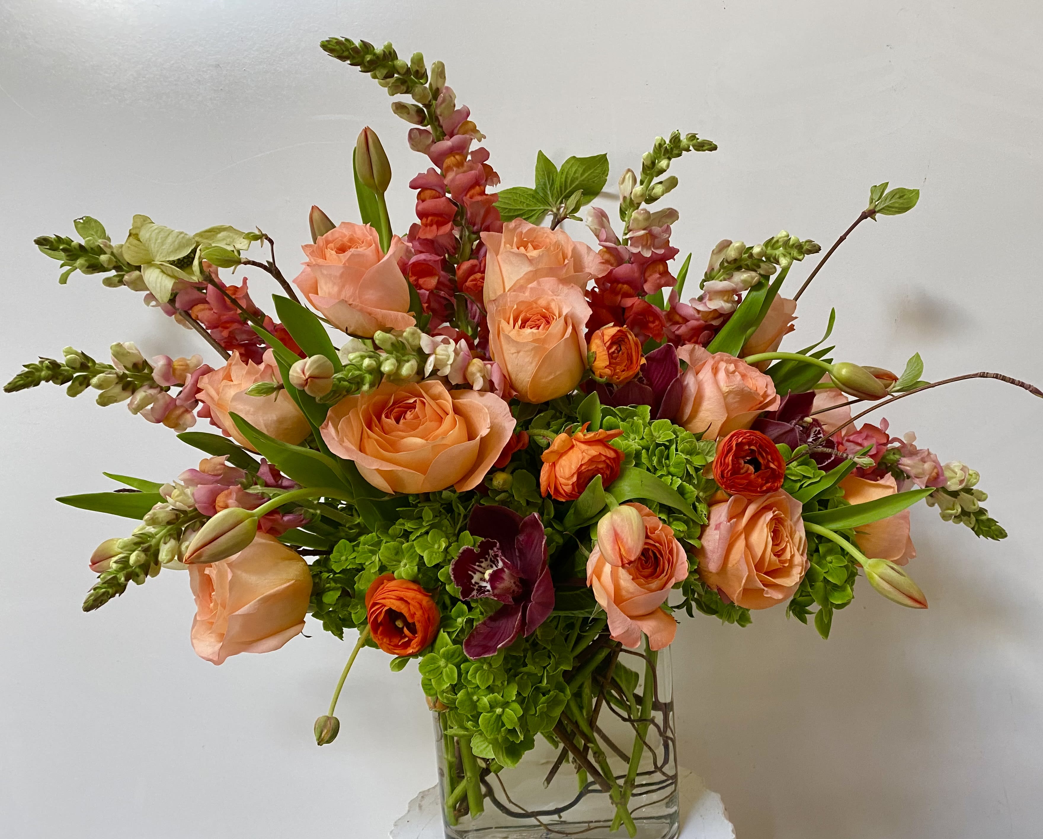 As Good As It Gets - orange roses in a glass vase with cymbidium and green hydrangeas 