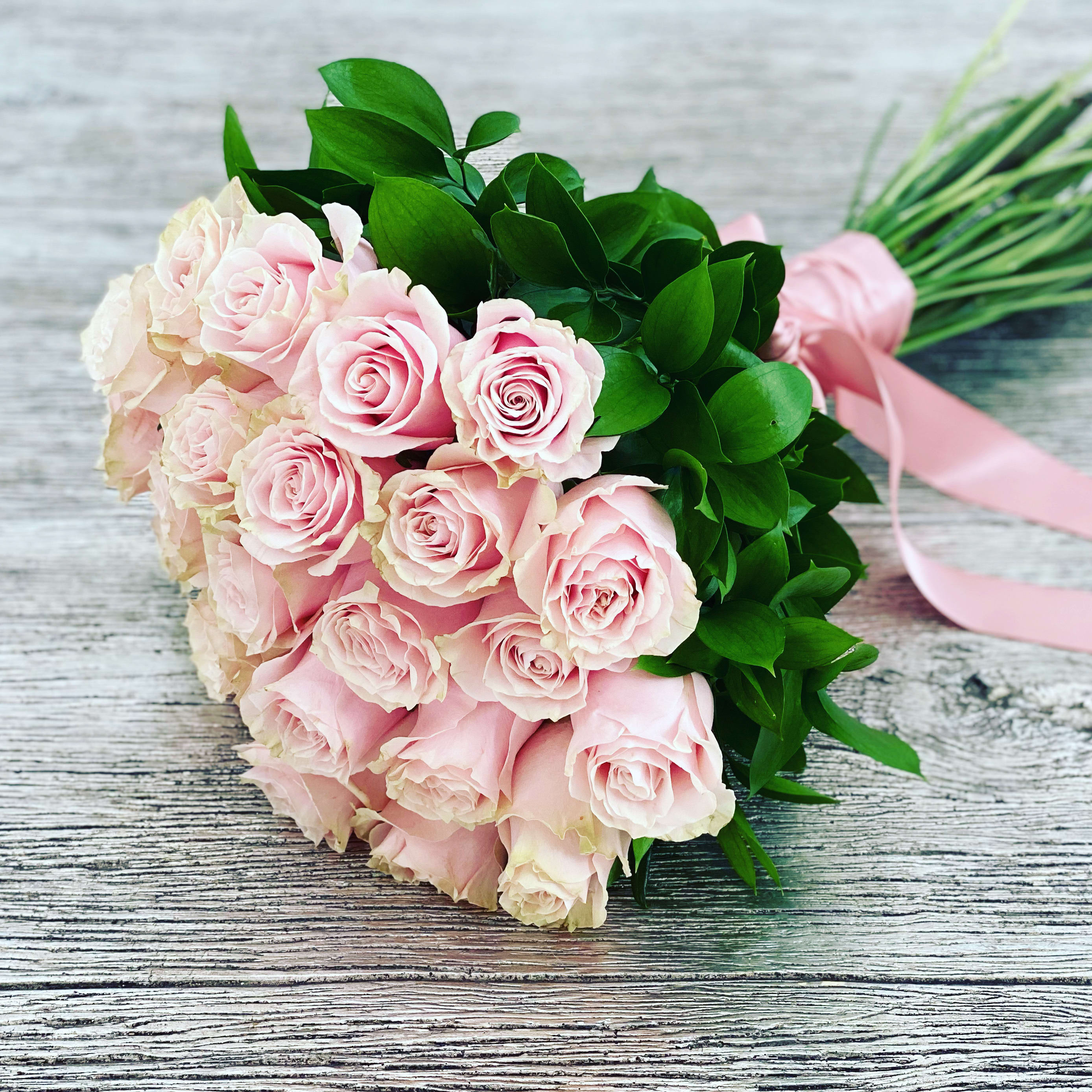 Two dozen long stem rose bouquet pink ™ - This bouquet features two dozen soft blush pink roses, gathered with lush greenery and tied with a satin ribbon. Romantic and elegant, it’s the perfect gesture of timeless beauty and charm.