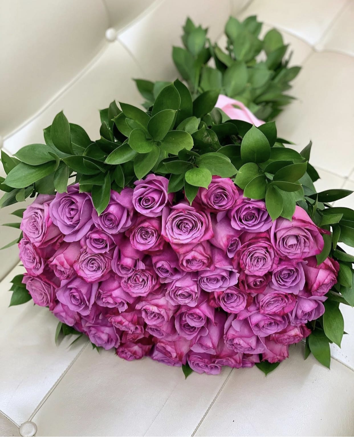 100 Purple Roses in hand tide bouquet ™ - This lavish bouquet showcases 100 radiant purple roses, gathered with lush greenery for a breathtaking display. Abundant and luxurious, it’s the ultimate statement of love, admiration, and elegance.