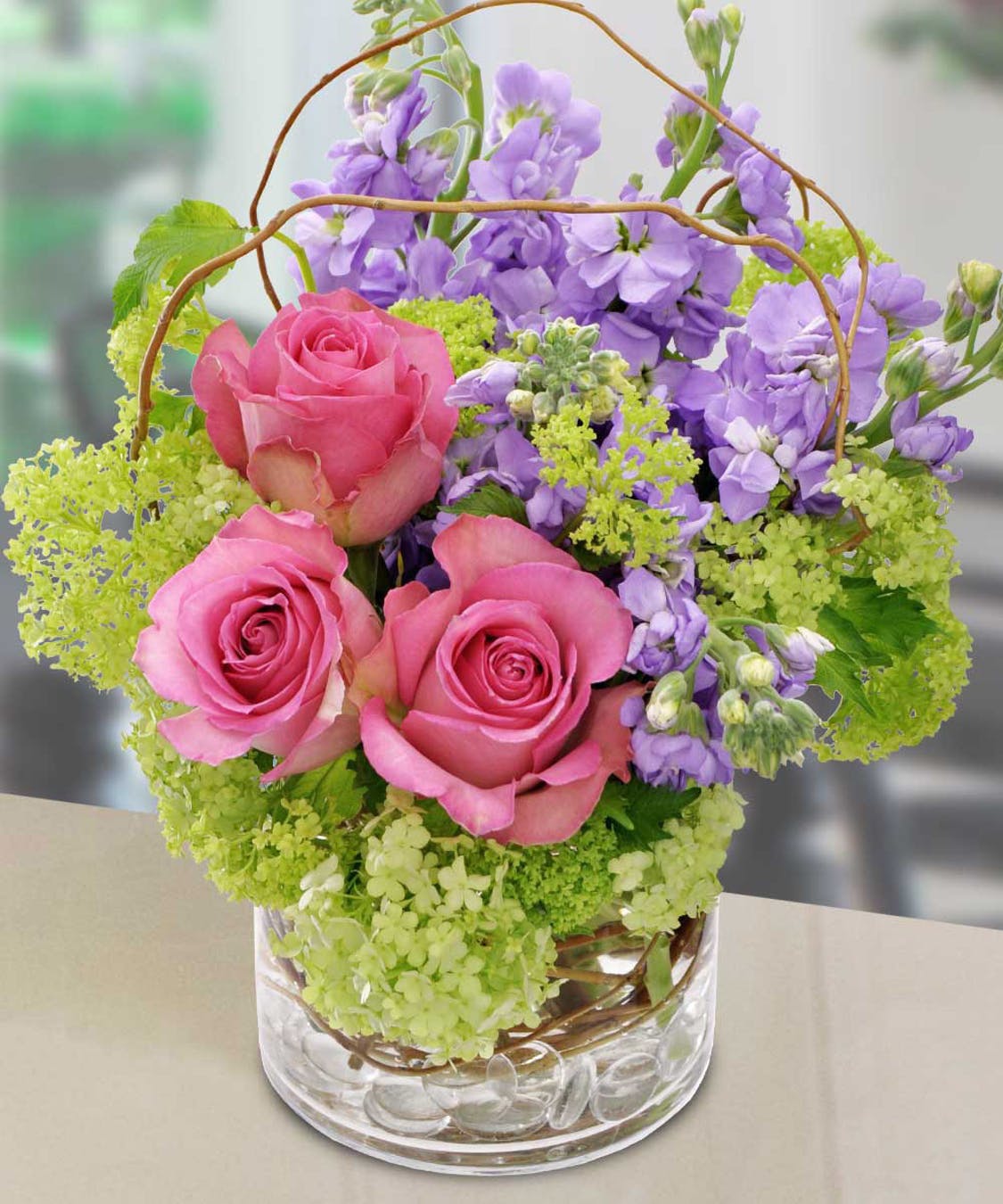 Pastel Meadows - Just a fresh breath of air is this very springy mix including pink roses, lavender stock and green miniature hydrangeas, accented by curly willow and arranged in a clear cylinder.