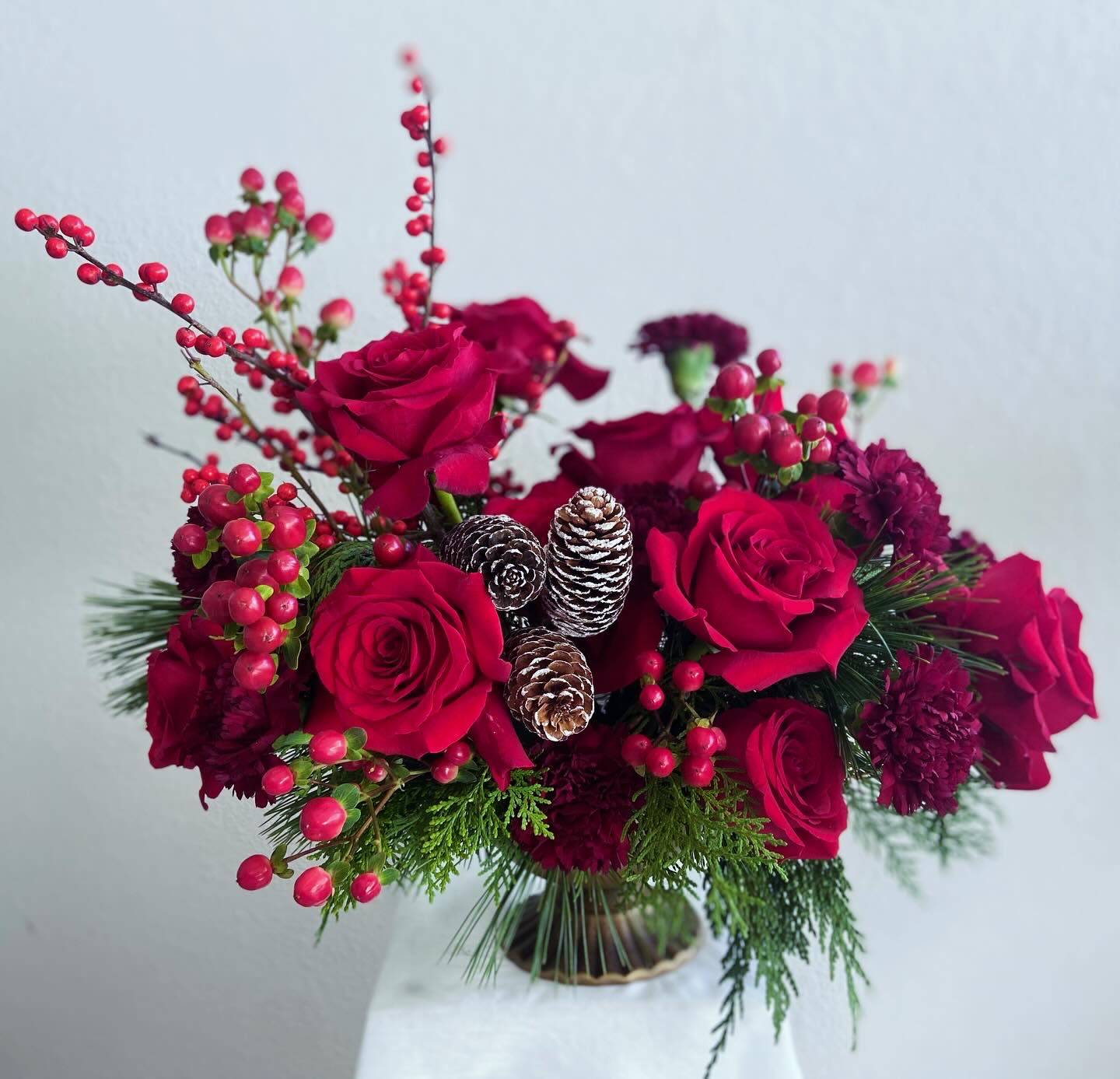 Scarlet Yuletide  - The “Scarlet Yuletide” is an April May Flowers original design. This captivating all-red floral arrangement radiates holiday cheer and warmth. This stunning bouquet features a harmonious mix of bold red carnations, luxurious red roses, and cheerful berries, all nestled among rich greenery and festive accents. Carefully arranged in a chic gold brushed compote, this arrangement creates a striking focal point that will brighten any room.   Perfect for holiday gatherings or as a heartfelt gift, Scarlet Yuletide embodies the joy and beauty of the season, making every moment feel a little more special. Celebrate the magic of Christmas with this enchanting floral masterpiece!
