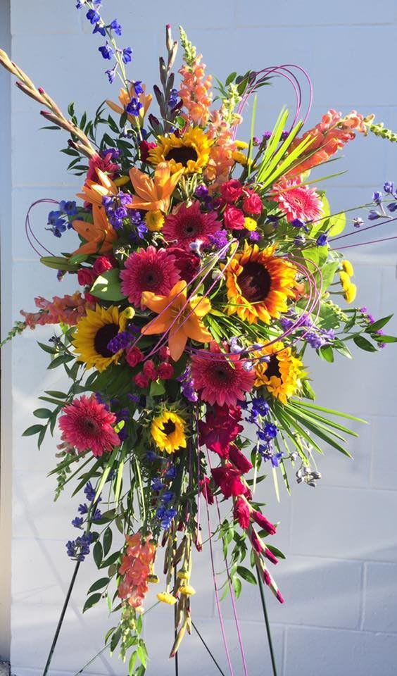 Summer Acres Standing Spray - Summer Acres Standing Spray is crafted with a mix of fuchsia, deep blue, hot pink and orange florals to celebrate their radiant life. This vibrant display combines bright shades with stunning texture while sharing thoughtful sentiments and comfort to loved ones.