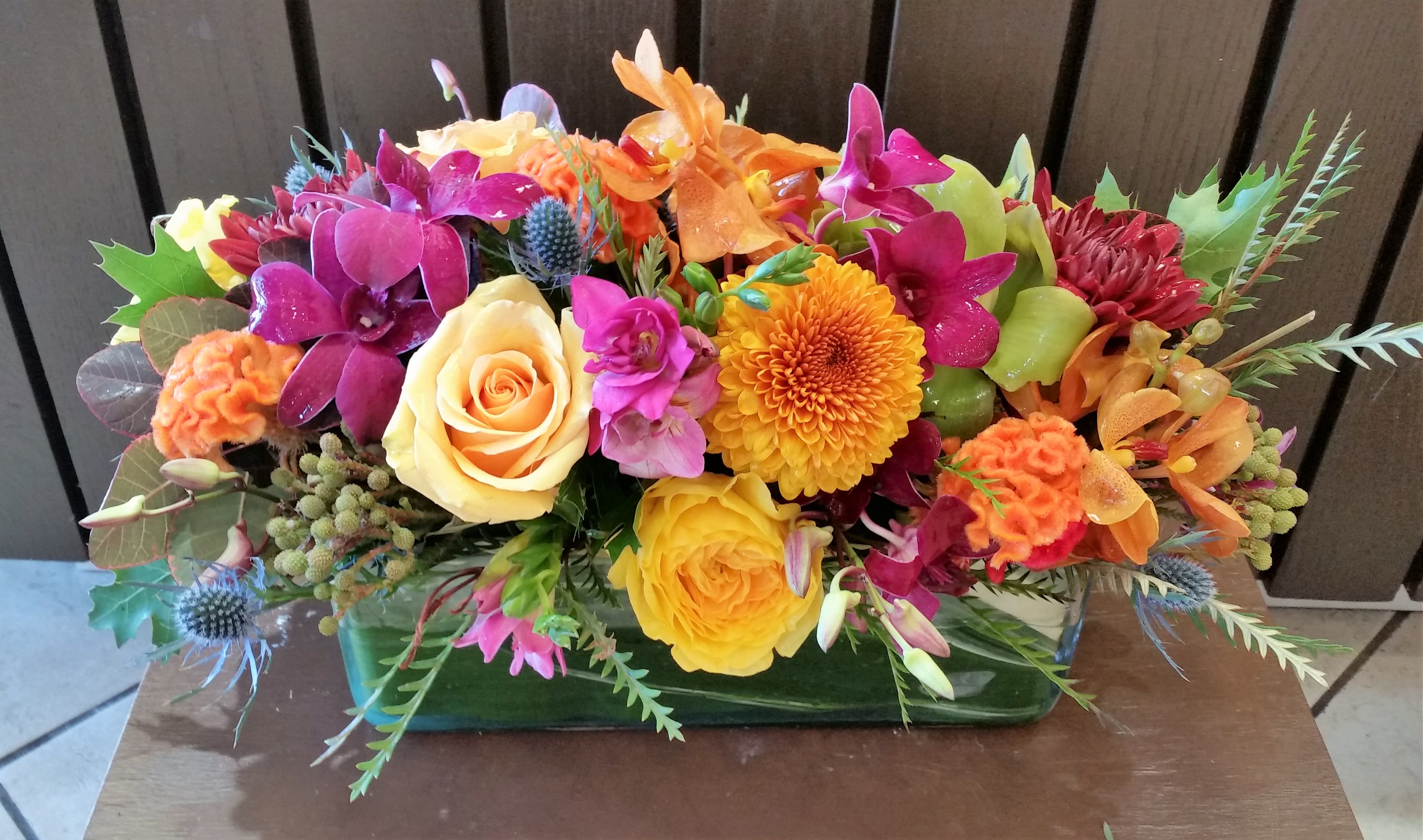 Mango Berry Crush - A lively combination of bright, upscale blooms including dendrobium and mokhara orchids, celosia, premium roses and textural accents, add pizzazz to your holiday table.  The best and the brightest in a large, clear glass rectangular vase lined with a variegated tropical leaf.  