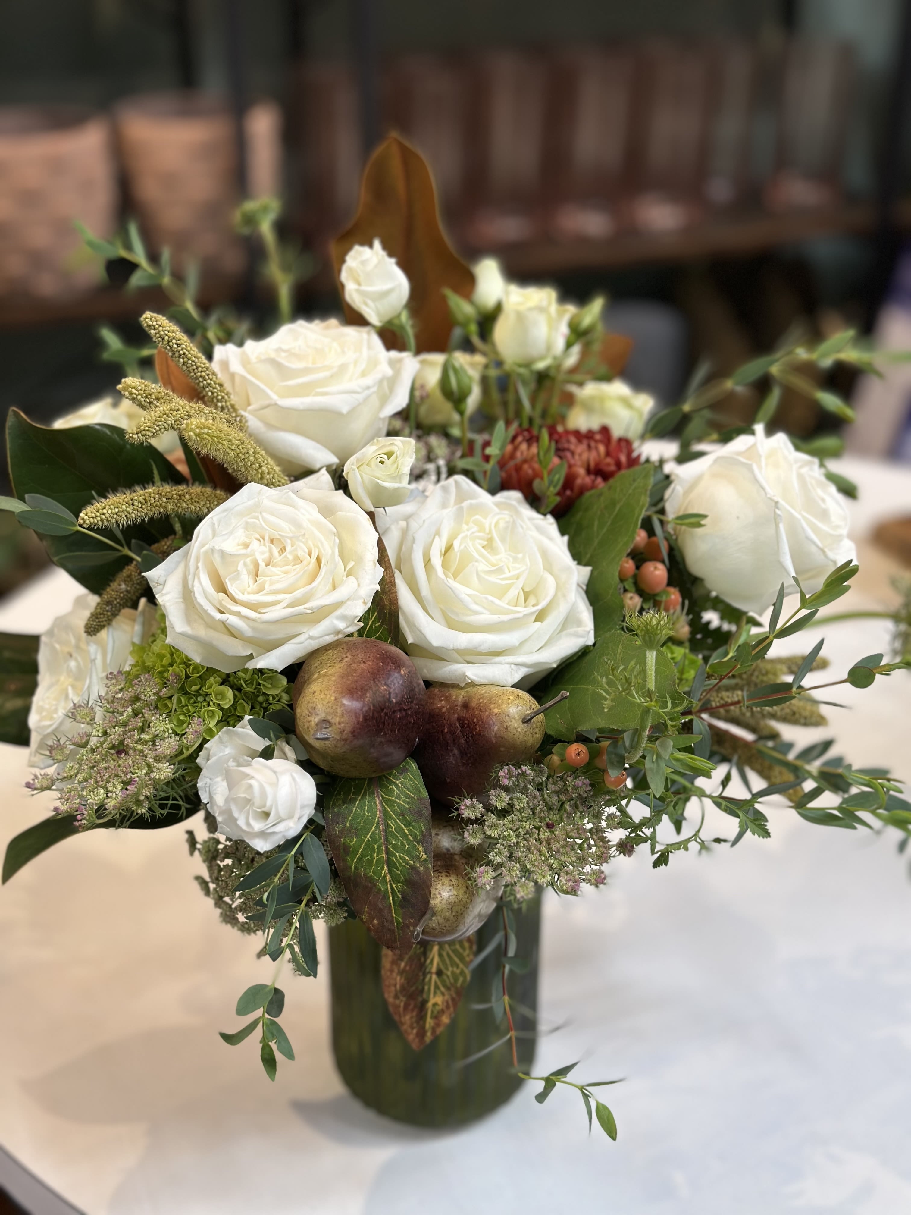 Rustic Elegance - Bring a touch of timeless sophistication to any space with Rustic Elegance. This lush arrangement pairs creamy white roses with textured seasonal greens, accented by warm earth tones for a natural harvest-inspired charm. Designed in a sophisticated glass fall colored vase, it's the perfect statement for fall gatherings, holiday tables, or as a refined gift that celebrates the beauty of the season. 