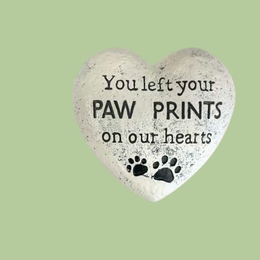  Paw Prints on Our Hearts Memorial Stone - Our Paw Prints on Our Hearts Memorial Stone is a touching tribute to the pets who left lasting love and joy in our lives. Crafted from weather-resistant resin with a natural stone finish, this heart-shaped keepsake features engraved paw prints and the heartfelt message, “You left your paw prints on our hearts.”  Perfect for garden memorials, pet gravesites, or indoor remembrance displays, this piece offers a comforting reminder of unconditional love that never fades.   Details: 	•	Measures approximately 6” wide 	•	Durable, outdoor-safe resin 	•	Subtle hand-finished texture for a natural stone look 	•	Suitable for dog or cat memorials 	•	Arrives beautifully packaged and ready for gifting