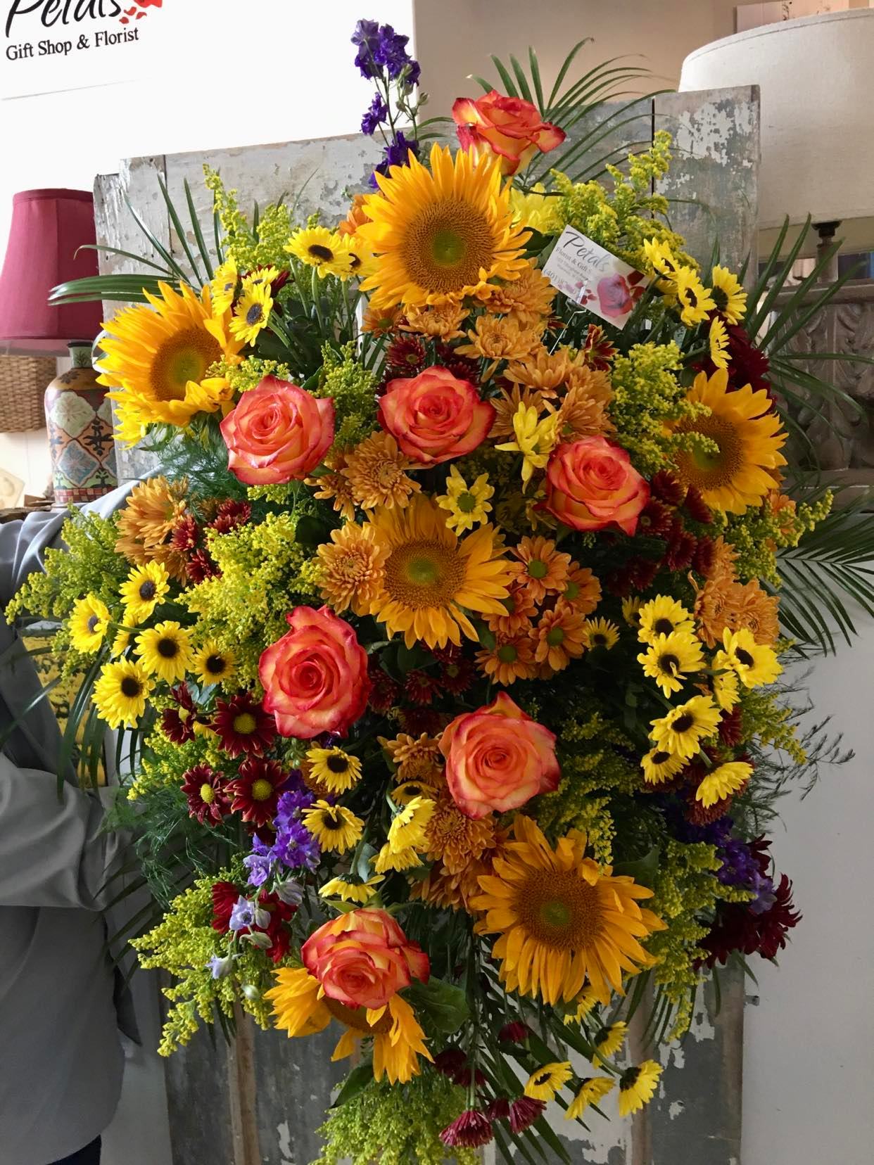 Autumn Harvest Standing Spray Tribute by Petals - This Autumn Harvest Standing Spray is a beautiful, showy seasonal tribute featuring a gorgeous array of fall flowers that include Assorted Chrysanthemums, Sunflowers, Stunning High &amp; Magic Roses, and Solidago  Please allow 24 to 48 hours for this design, as we need this time to order and process your fresh flowers.  If you require same-day delivery or are placing your order after 12:00 PM, please call Cheryl directly at 401-828-0701 to confirm availability. 