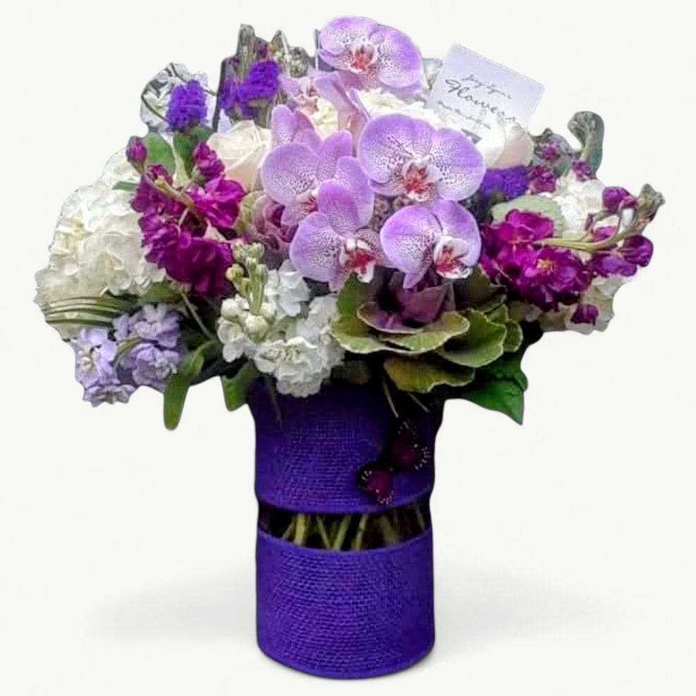 Luxe Violet Orchid Beauty - Tall Designer Vase - Layers of exquisite violet, lilac and white blooms are designed in a tall, couture wrapped vase for a dramatic, unforgettable presentation. Fresh premium orchids, lush hydrangea and elegant seasonal blooms create this rich, romantic color story that always feels extraordinary.