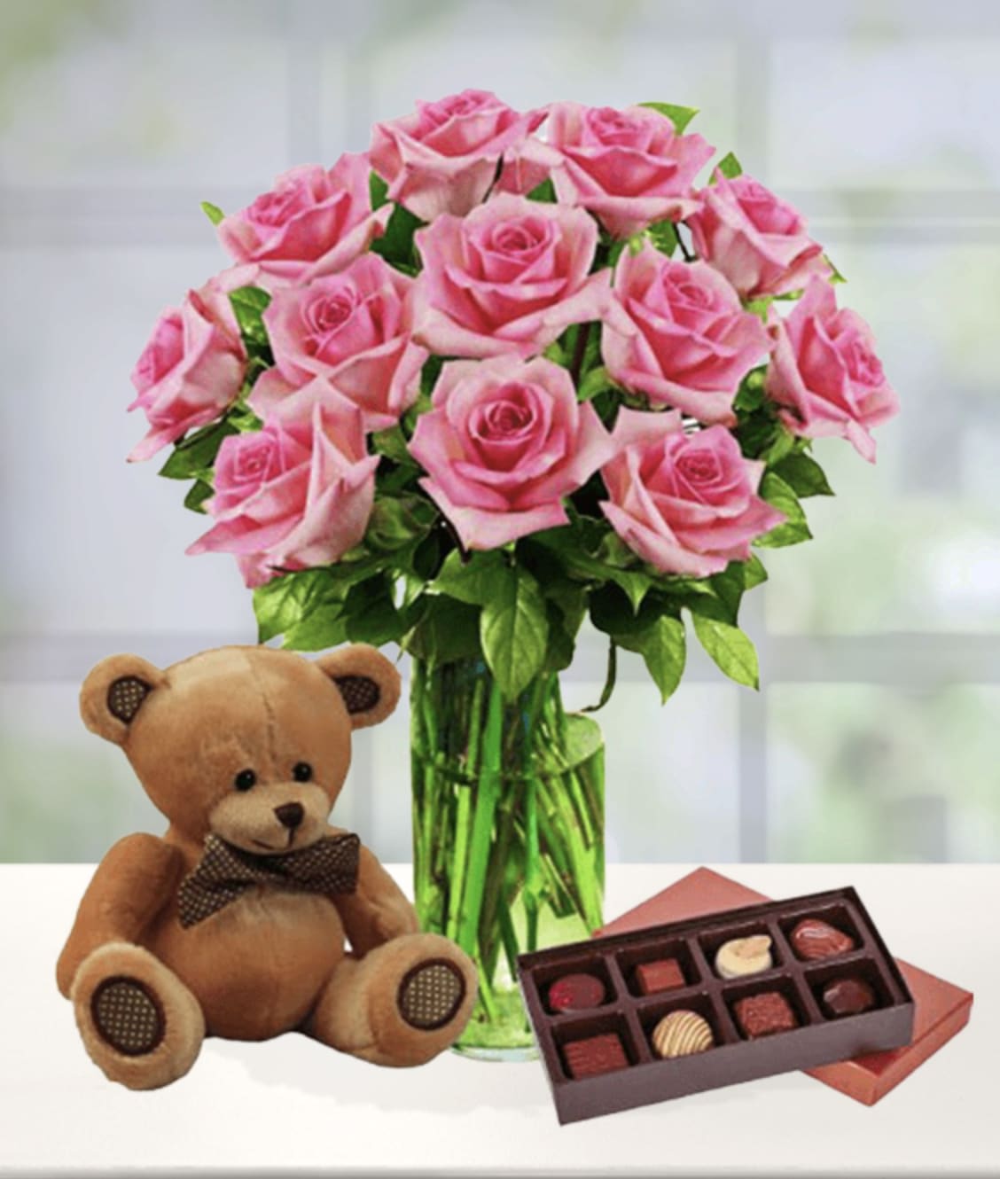 12 Pink Roses, Bear &amp; Chocolates - One dozen pink roses is a lovely arrangement to send any time of the year. Pair it with an adorable plush bear and a delicious box of chocolates, it's a gift that is sure to impress.  Item pictured is a depiction of an arrangement that we will make as similar as possible with the same look and feel.