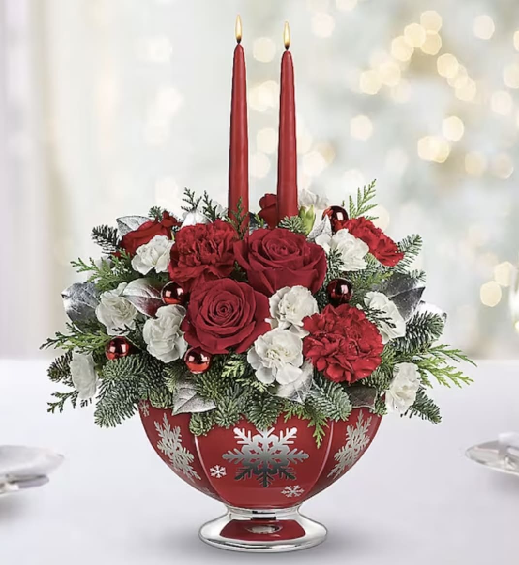 SILVER AND JOY CENTERPIECE - Make the season bright with shimmering snowflakes, glowing tapers and radiant holiday blooms. This elegant, hand-glazed ceramic bowl sparkles with silver snowflakes beneath beautiful red roses, carnations and winter greens. The food-safe design will long bring joy to their holiday table! Lush red roses, red carnations and white miniature carnations are arranged with lemon leaf, flat cedar and noble fir. Delivered in a Silver And Joy bowl.