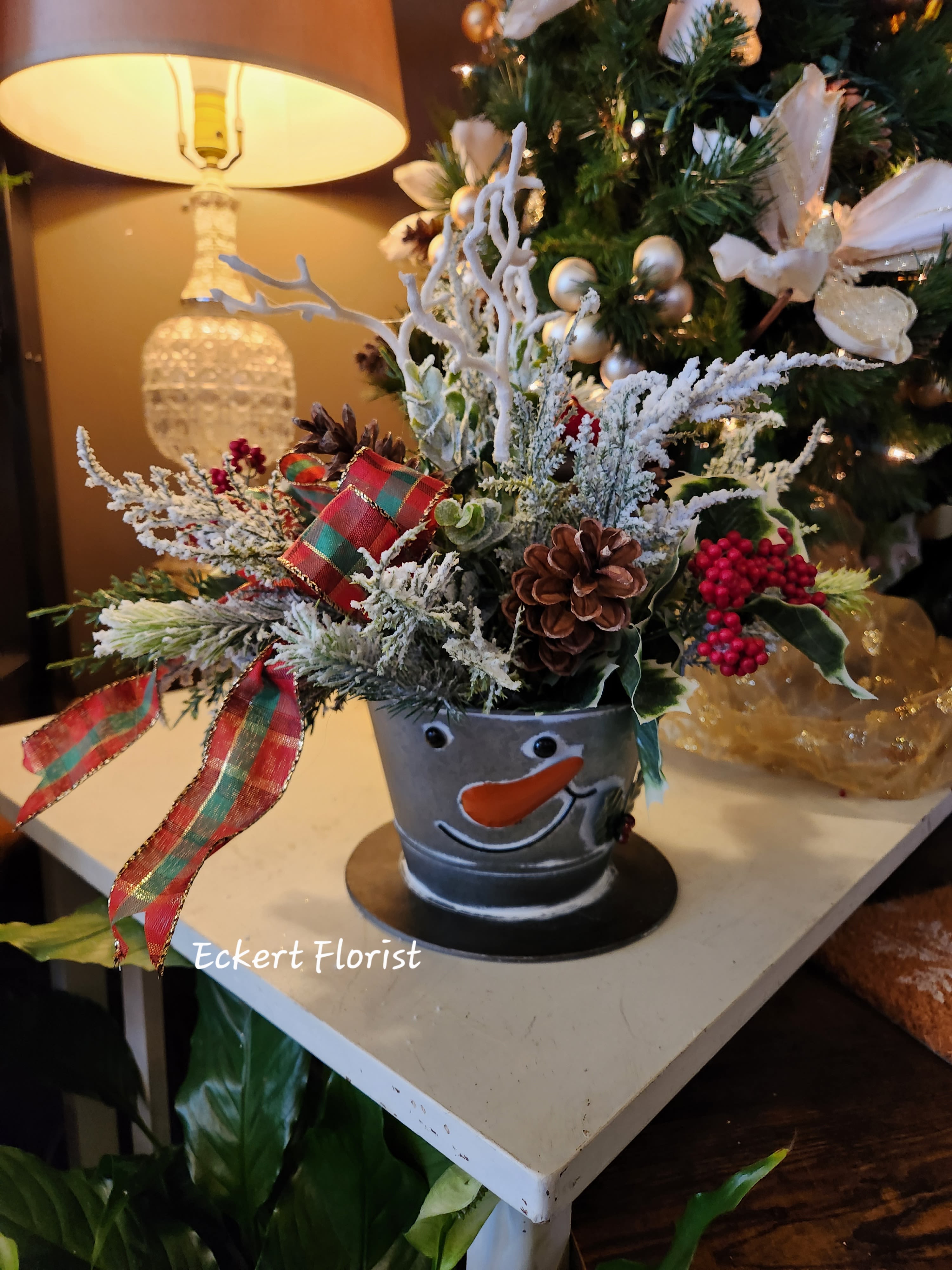 Eckert Florist's Artificial Tin Snowman Tophat Bouquet *Our Local Delivery Only - This Artificial Christmas arrangement is So Cute it will bring a smile to anyone's face!!!  Tin measures approx: 7&quot; Diameter x 4.5&quot; High *Our local delivery only