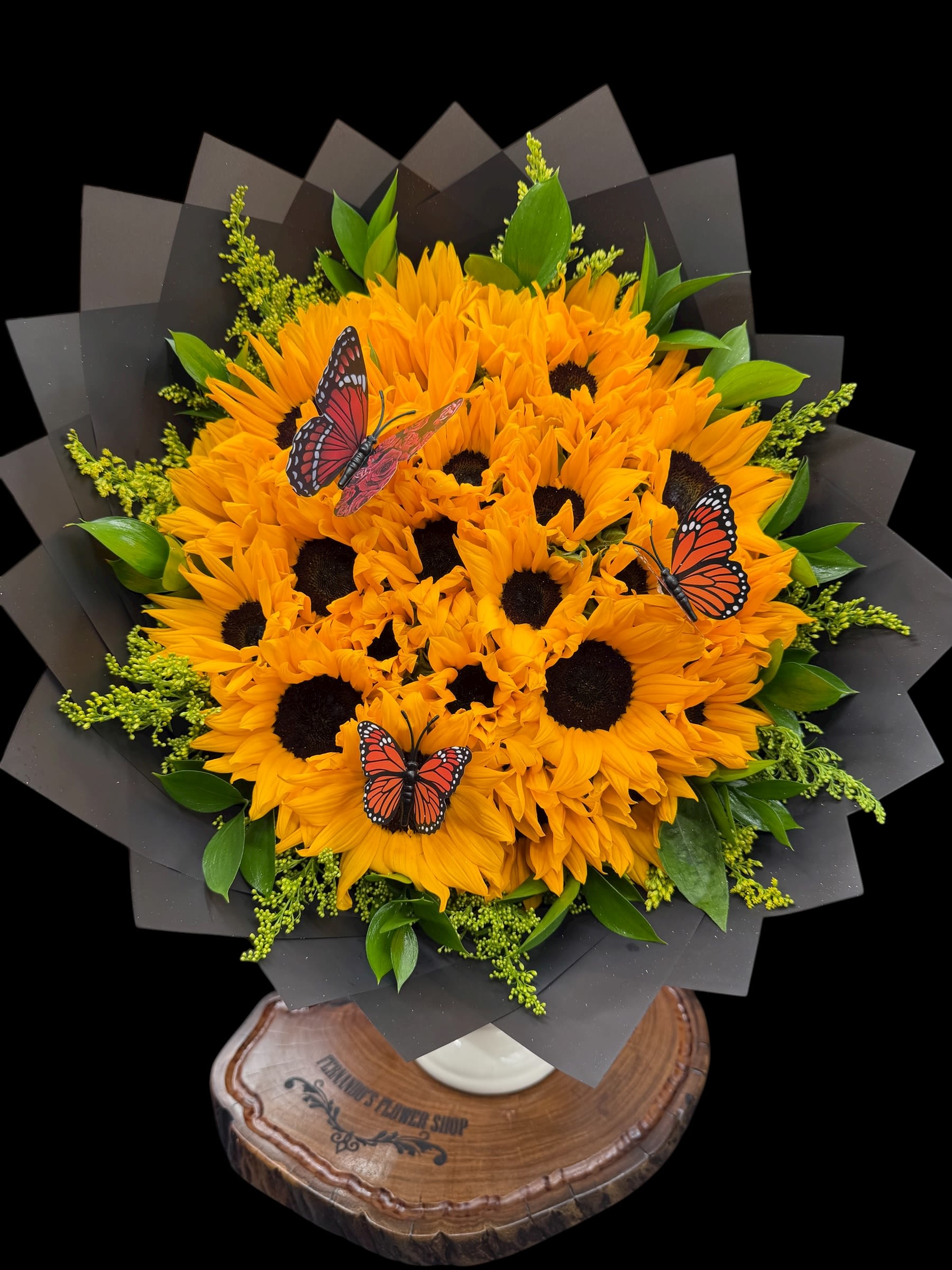 25 Sunflowers - A radiant bouquet of 25 vibrant sunflowers, symbolizing happiness, strength, and positivity. Accented with lush greenery and delicate butterflies, this design brings pure sunshine to any moment. Perfect for brightening someone’s day or celebrating life’s joyful occasions. 
