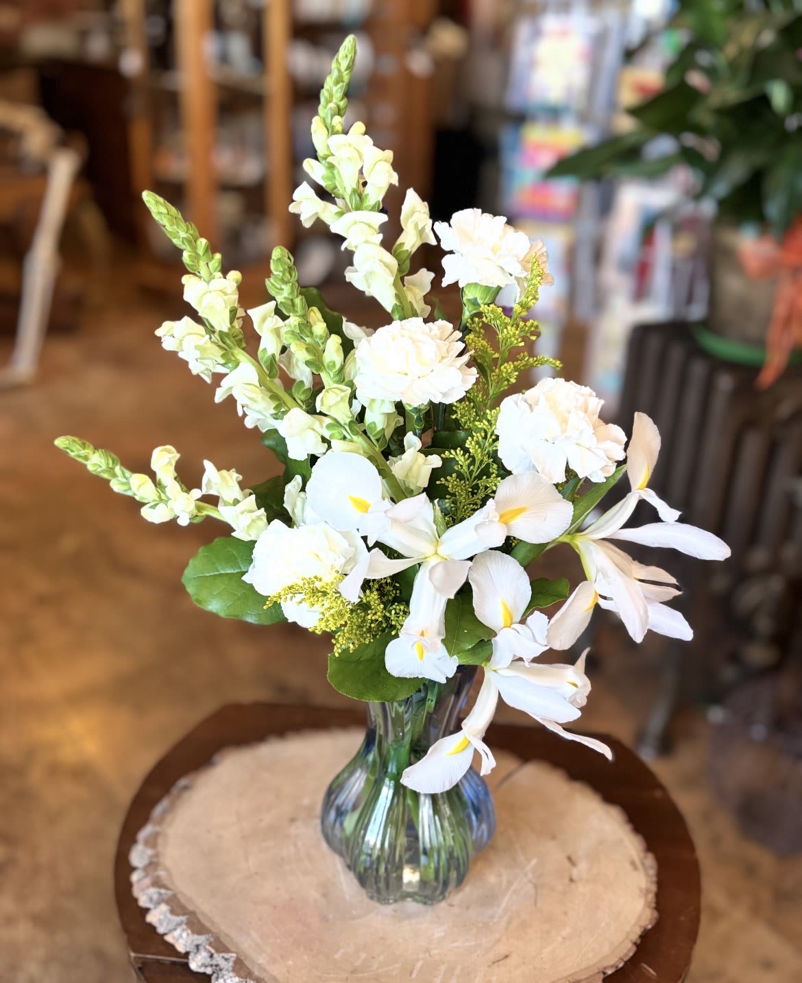 Quiet Moments  - When words aren’t enough, let the calm beauty of white bloom hues of blue bring comfort. A peaceful way to honor memories and share quiet moments of reflection.  Standard arrangement content: White iris, white snaps, white carnations, assorted greenery and solid aster arranged in a light blue vase. 