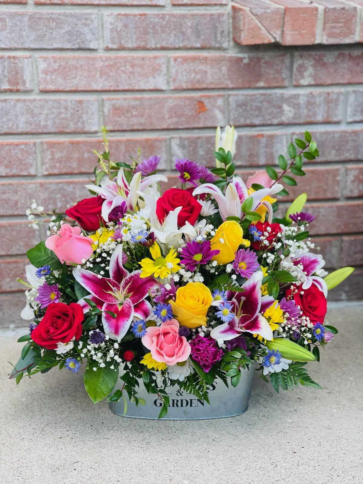 Kaleidoscope Basket - A kaleidoscope of colors fills this arrangement to the brim in a silver basket! Elegant lilies, cheerful daisies, classic roses, and more create a vibrant burst of color and joy.