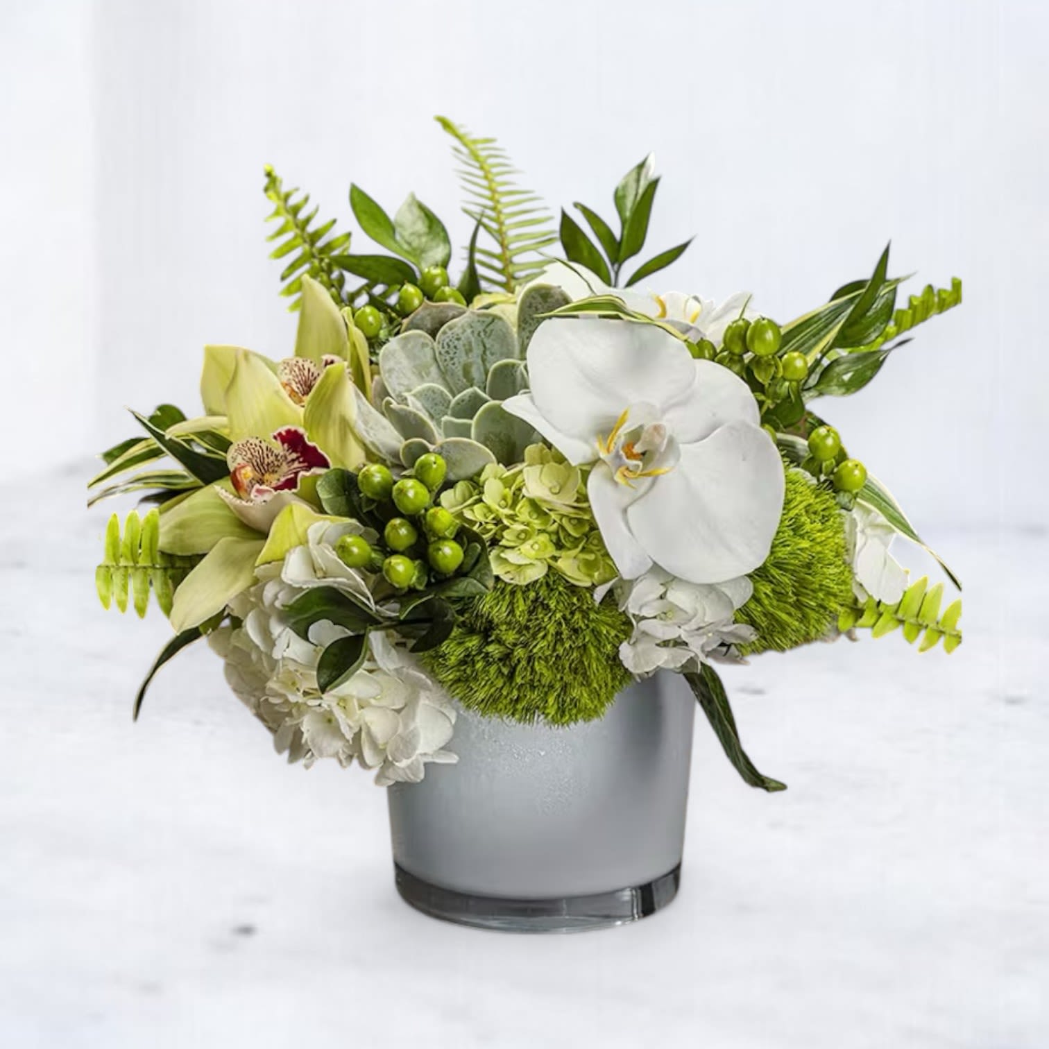 Emerald Oasis - Step into a world of serene elegance with the Emerald Oasis arrangement. Featuring exquisite white phalaenopsis orchids, vibrant green cymbidium orchids, lush moss, and delicate succulents, this design captures the essence of natural beauty. Accented with fresh greenery and nestled in a modern vase, this arrangement is perfect for expressing gratitude, or adding a touch of sophistication to any space. Available for same-day delivery in Houston and surrounding areas, the Emerald Oasis brings a tranquil charm to any occasion.