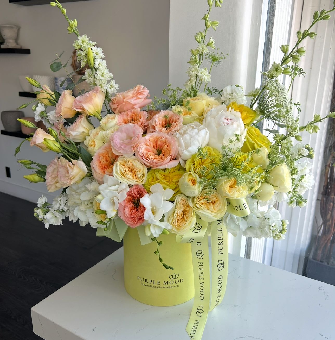 Limoncello Box - Container size - D6.75'x H7.5'  Bright and joyful, the Limoncello Box is bursting with sunshine colors of yellow, orange, pink, and white. Styled in a bold yellow hat box, this arrangement brings happiness and energy to any celebration. Perfect for birthdays, thank-yous, or simply to make someone’s day brighter.  Key Features:     •    Presented in a vibrant yellow hat box for a cheerful look     •    Finished with signature ribbon for an elegant detail     •    Filled with colorful blooms to spread joy and positivity     •    A radiant gift for any happy occasion