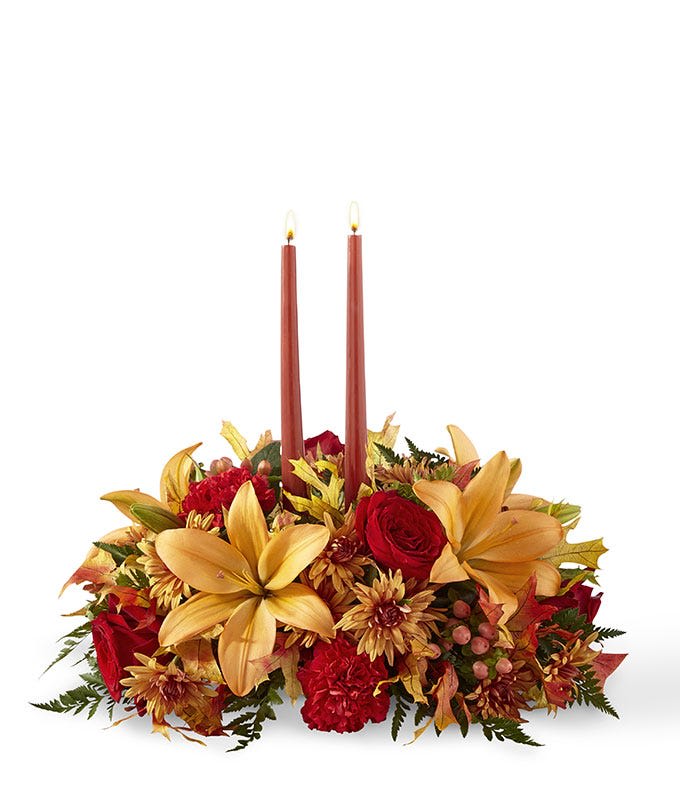 Autumn Lights Centerpiece - Fall is all about coming together and making memories with one another. The Autumn Lights Centerpiece helps make those precious moments even more special. With red roses, peach Asiatic lilies and red carnations and bronze cushion poms embracing 2 taper candles, this centerpiece is a beautiful gift for every Autumn occasion.