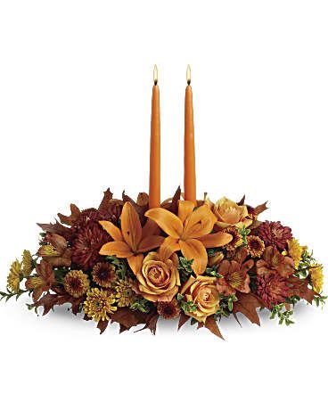 The Gathering Centerpiece - Graciously gather your family around the warm glow and classic autumn colors of this stunning Thanksgiving centerpiece. A lush variety of burnt orange blooms are gathered under a pair of tall, graceful candles - perfect for decorating your Thanksgiving dinner table, entryway or hearth. Fall flowers include orange roses, orange lilies, dark orange alstroemeria, bronze button mums, yellow cushion mums, rust cushion mums, and green huckleberry. Accented with oak leaves and two orange taper candles.