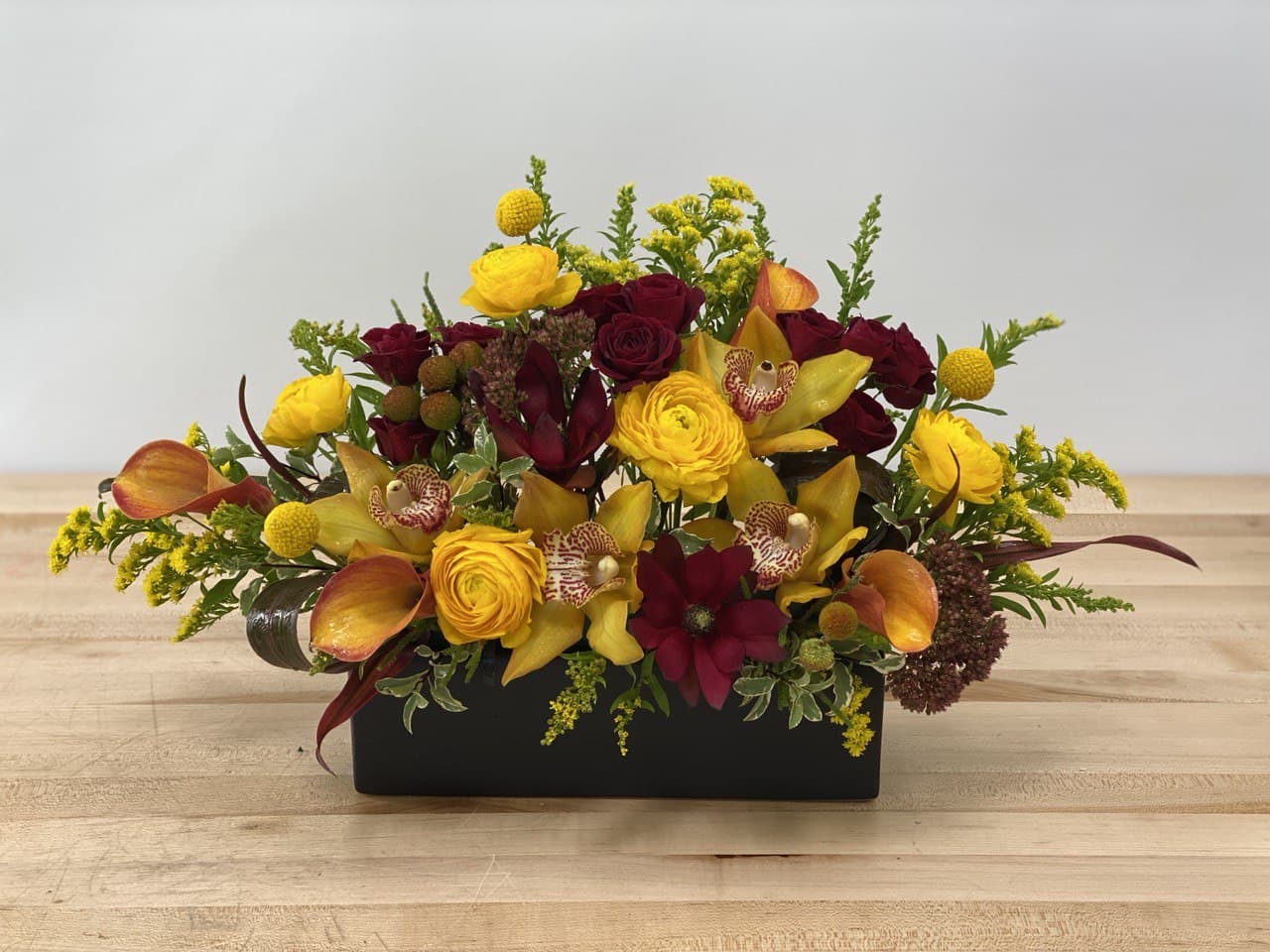 Fire Blooms - This sophisticated design and bold color combination of cymbidium orchids, spray roses, calla lilies, and ranunculus in fall colors is an ideal statement or holiday centerpiece.