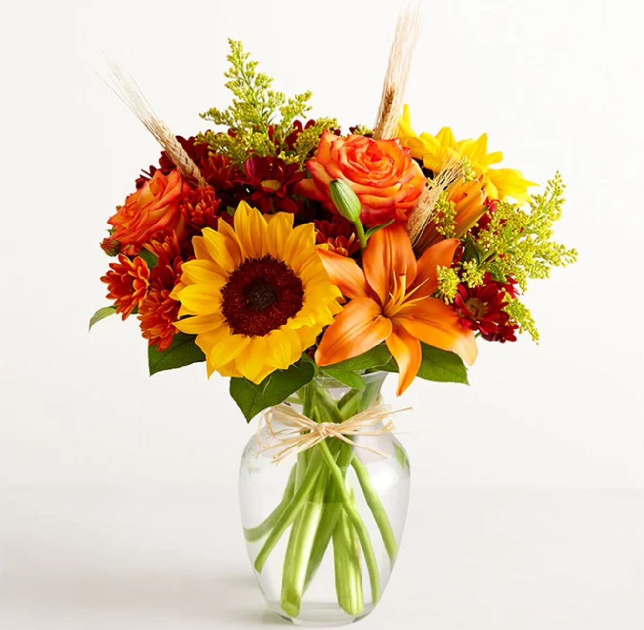 Fields of Europe® for Fall - All-around arrangement with sunflowers, autumn-color roses, sunflowers, orange Asiatic lilies, and red and rust-color daisy poms, accented with wheat and assorted greenery Artistically designed in a clear glass vase accented with raffia; measures 8&quot;H Premium arrangement measures approximately 18&quot;H x 14&quot;W Deluxe arrangement measures approximately 17&quot;H x 13&quot;W Standard arrangement measures approximately 16&quot;H x 12&quot;W